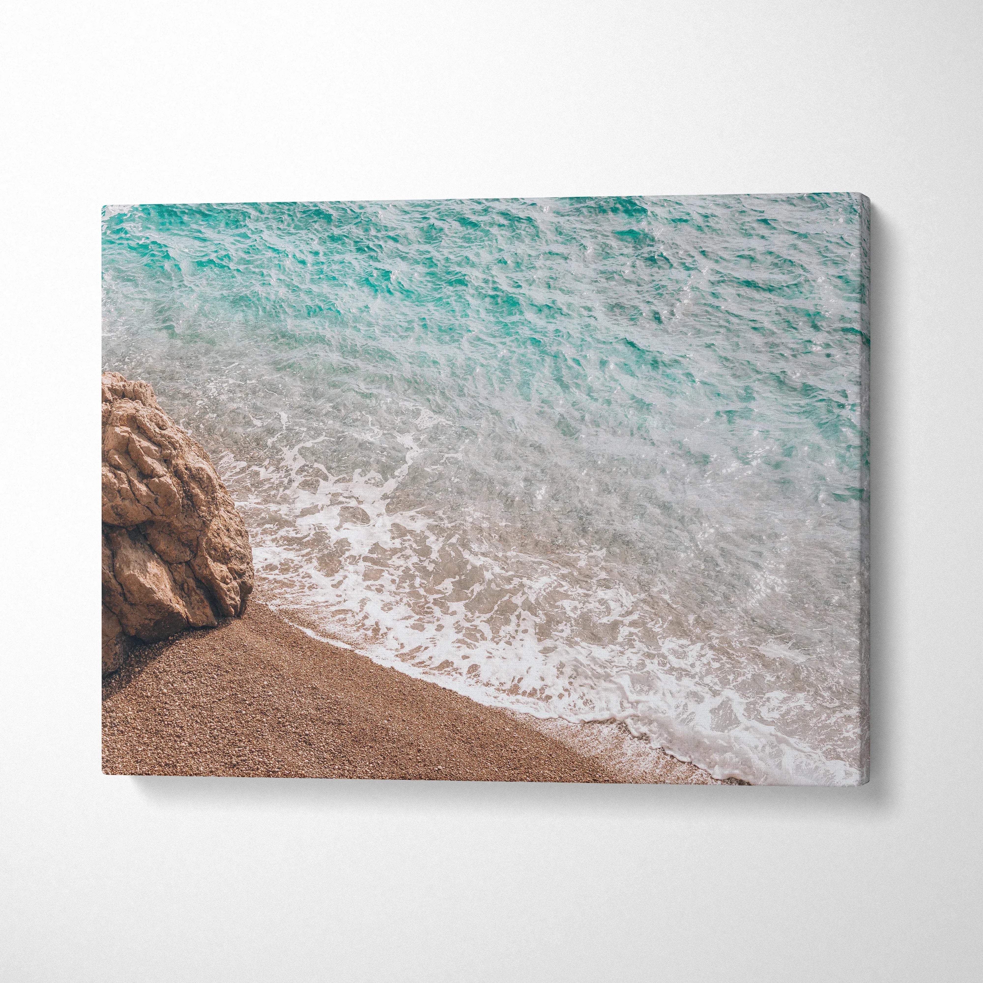 Beige canvas print of turquoise ocean waves on sandy shore by rocks