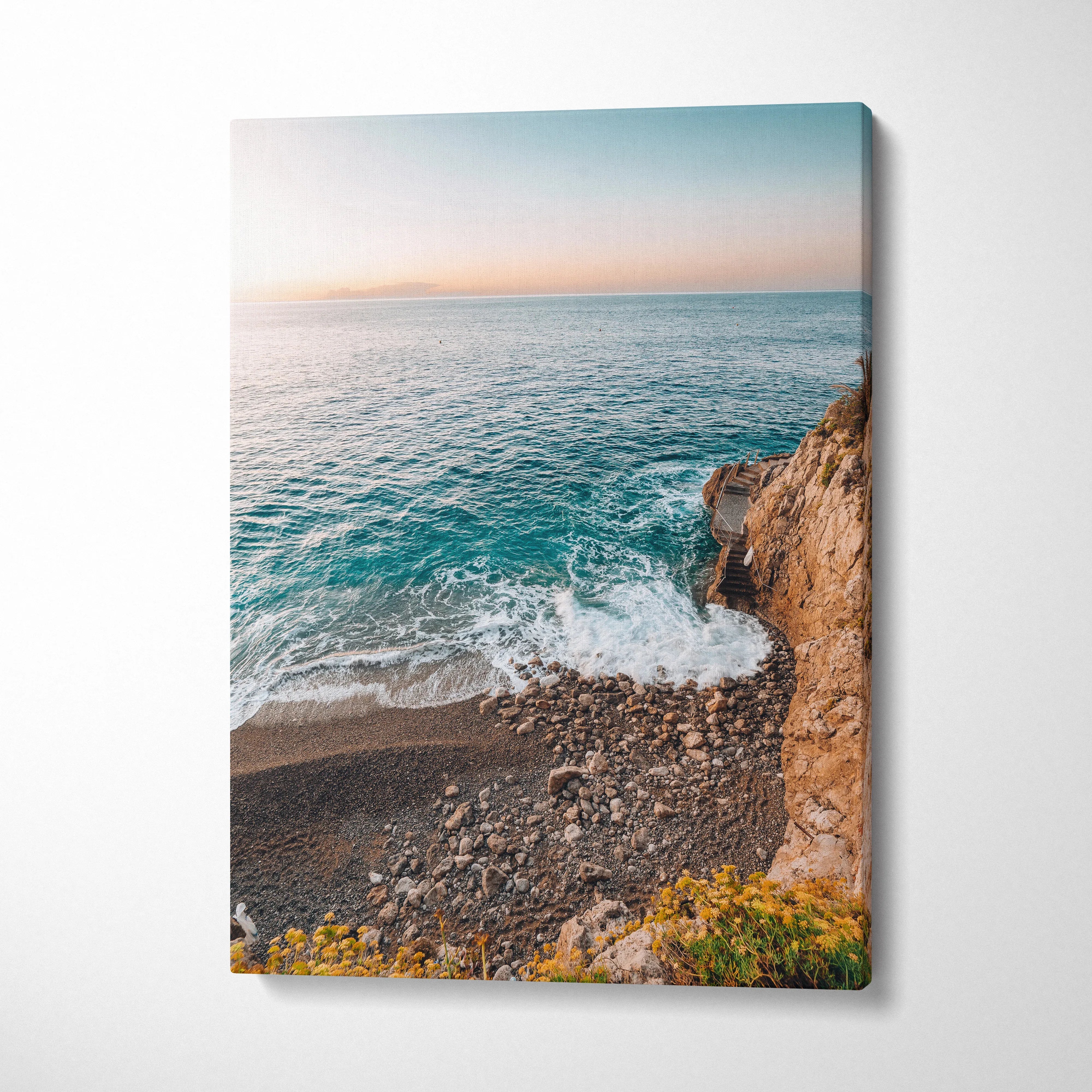 Canvas wall art featuring a serene beach scene with turquoise waves crashing against rocky cliffs under a soft pastel sky.