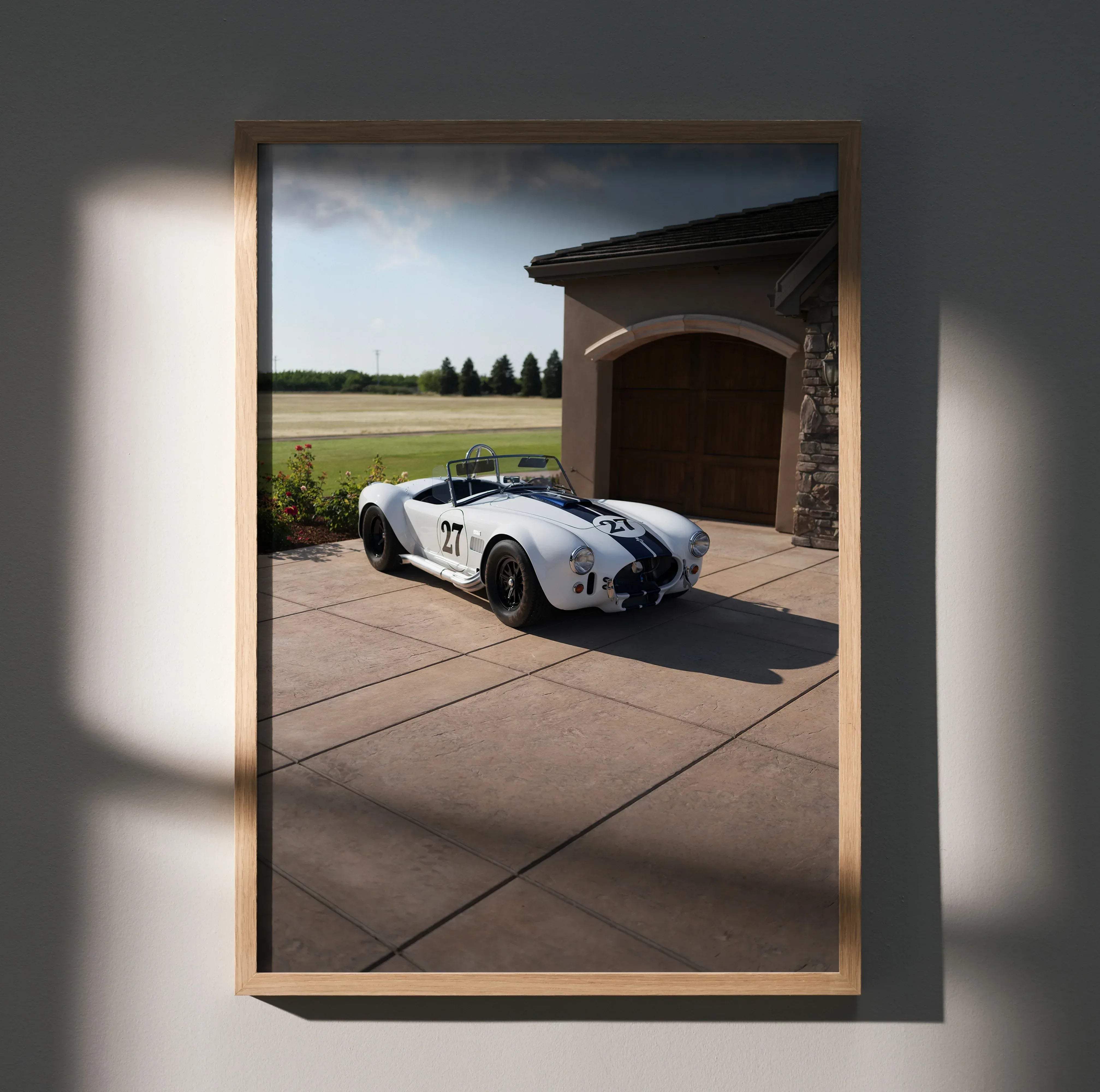 A framed high resolution Shelby Cobra car poster featuring a white and black racing car number 27 parked by a garage