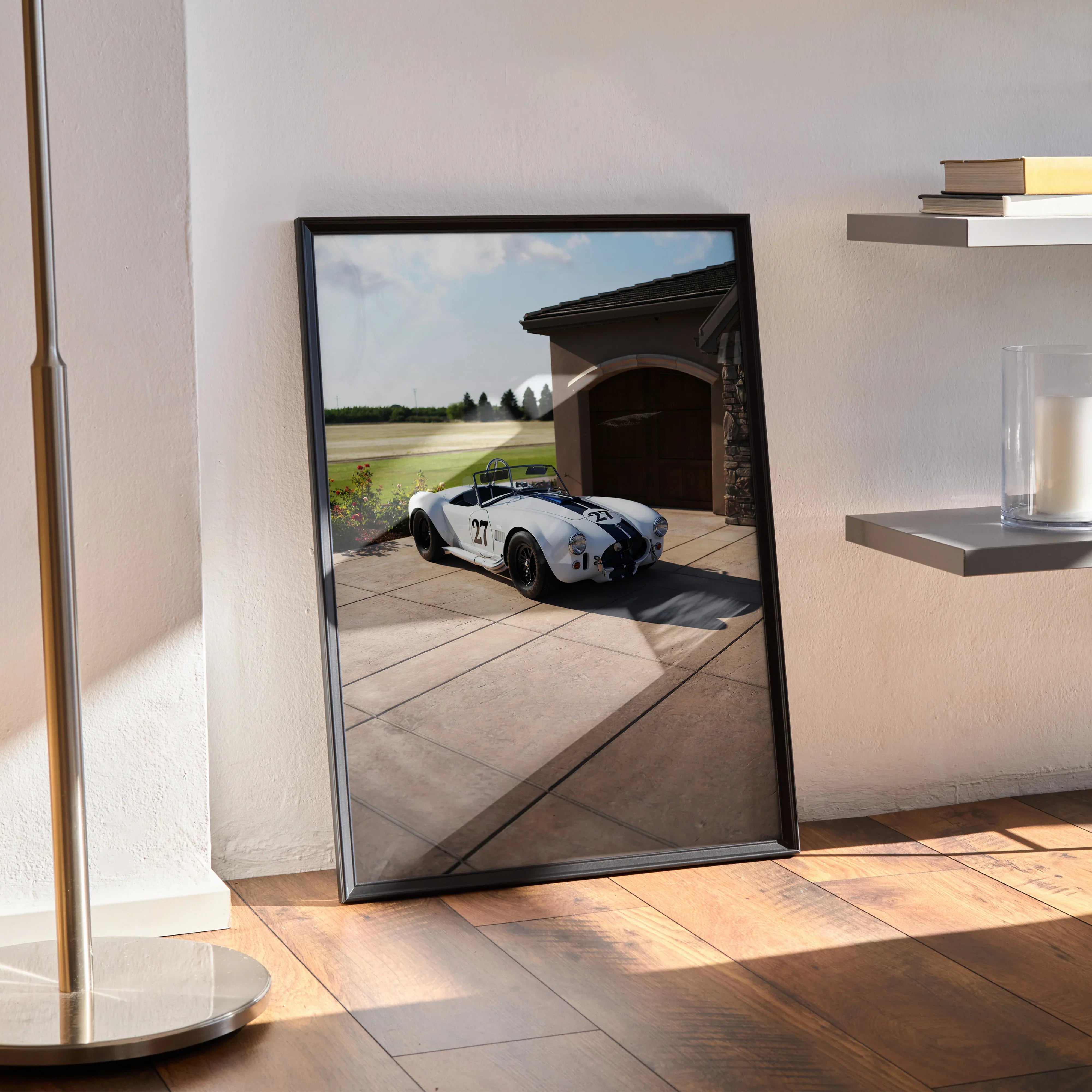 Shelby Cobra car poster wall art with black frame leaning against white wall on wooden floor.