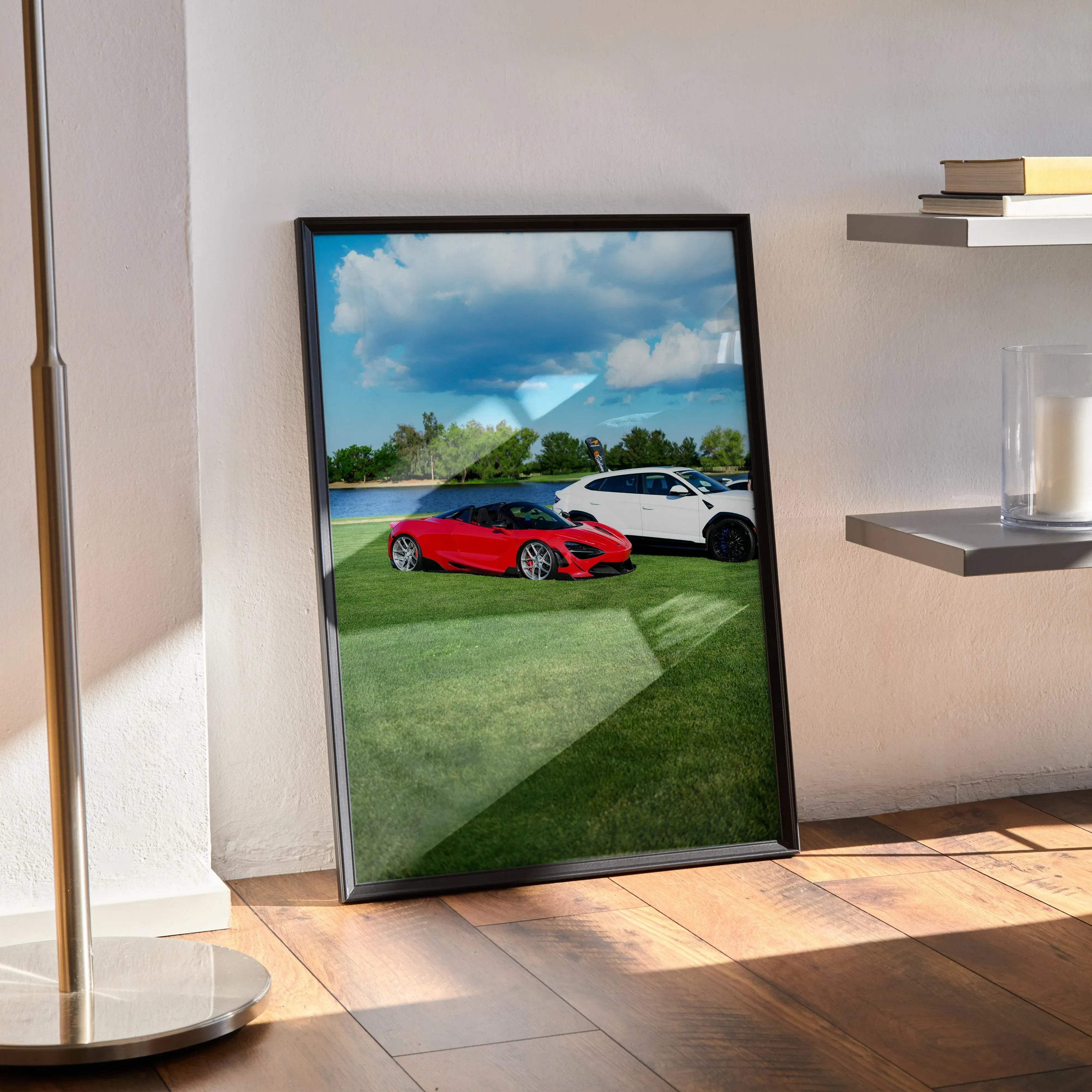 Black-framed poster featuring a vibrant red mclaren 720s sports car and white suv on green grass under blue sky clouds