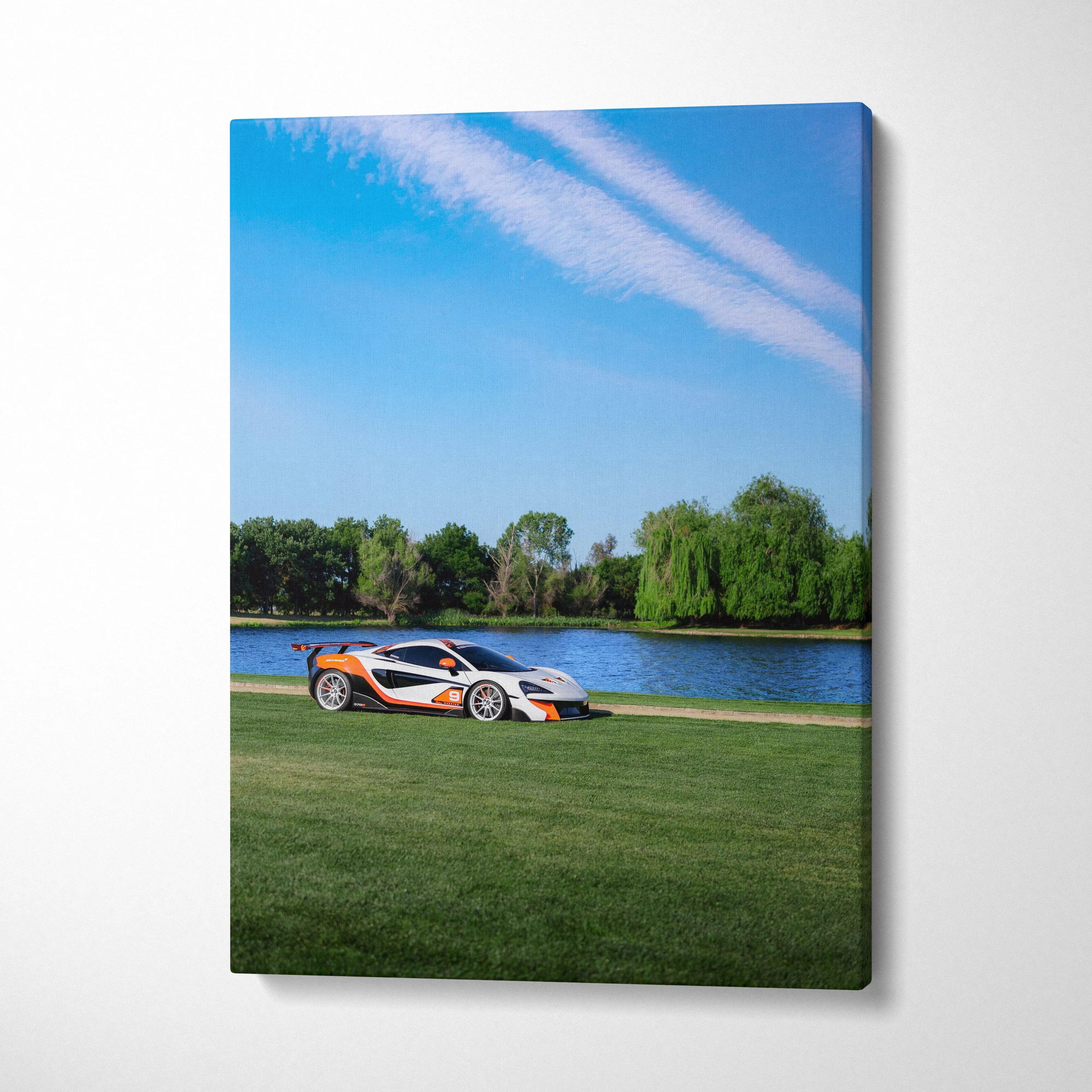 Vertical canvas wall art featuring a McLaren 570S on green grass by a lake under blue sky.