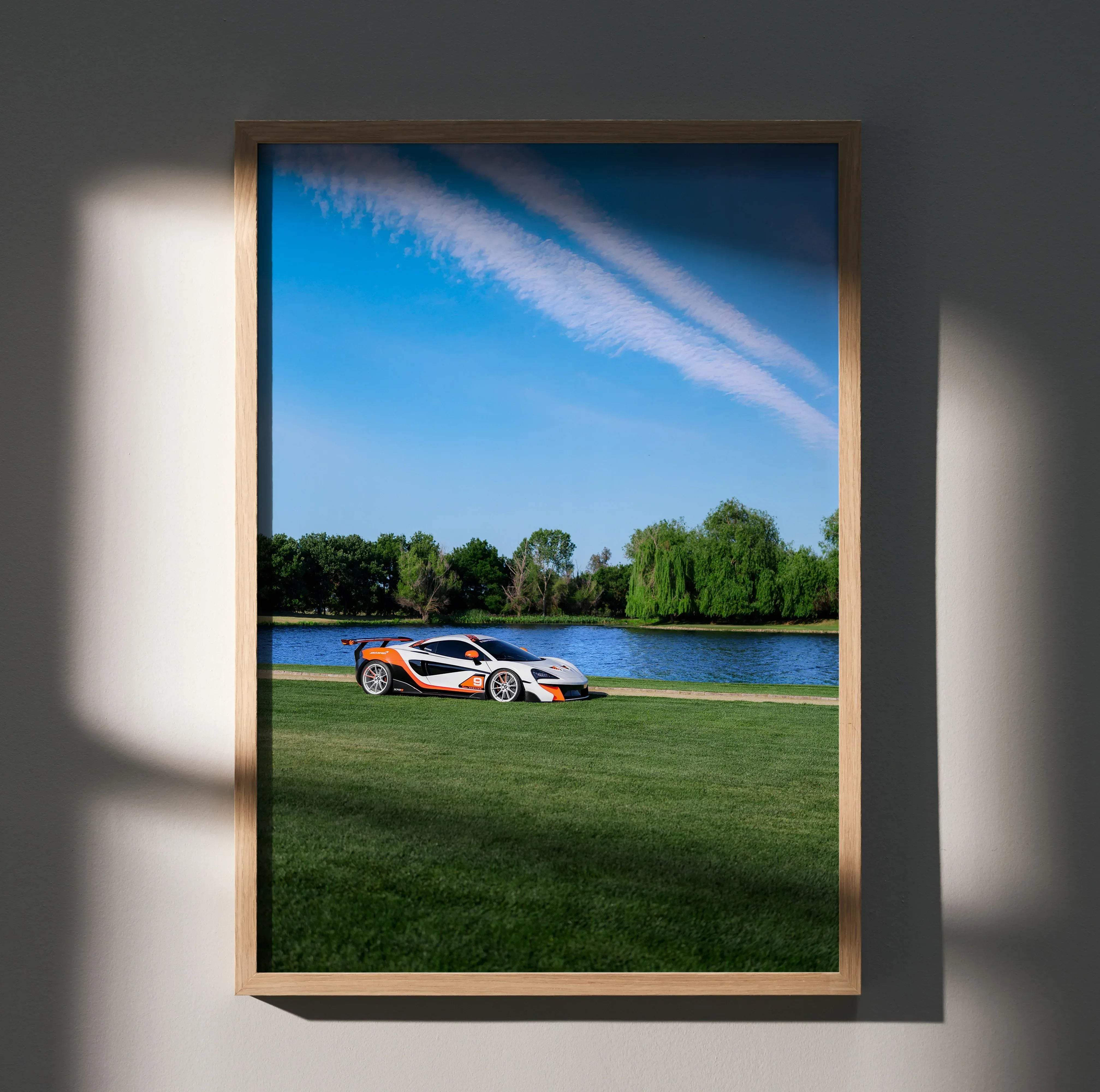 A framed high resolution photo poster of a white and orange McLaren 570S sports car parked by a lake