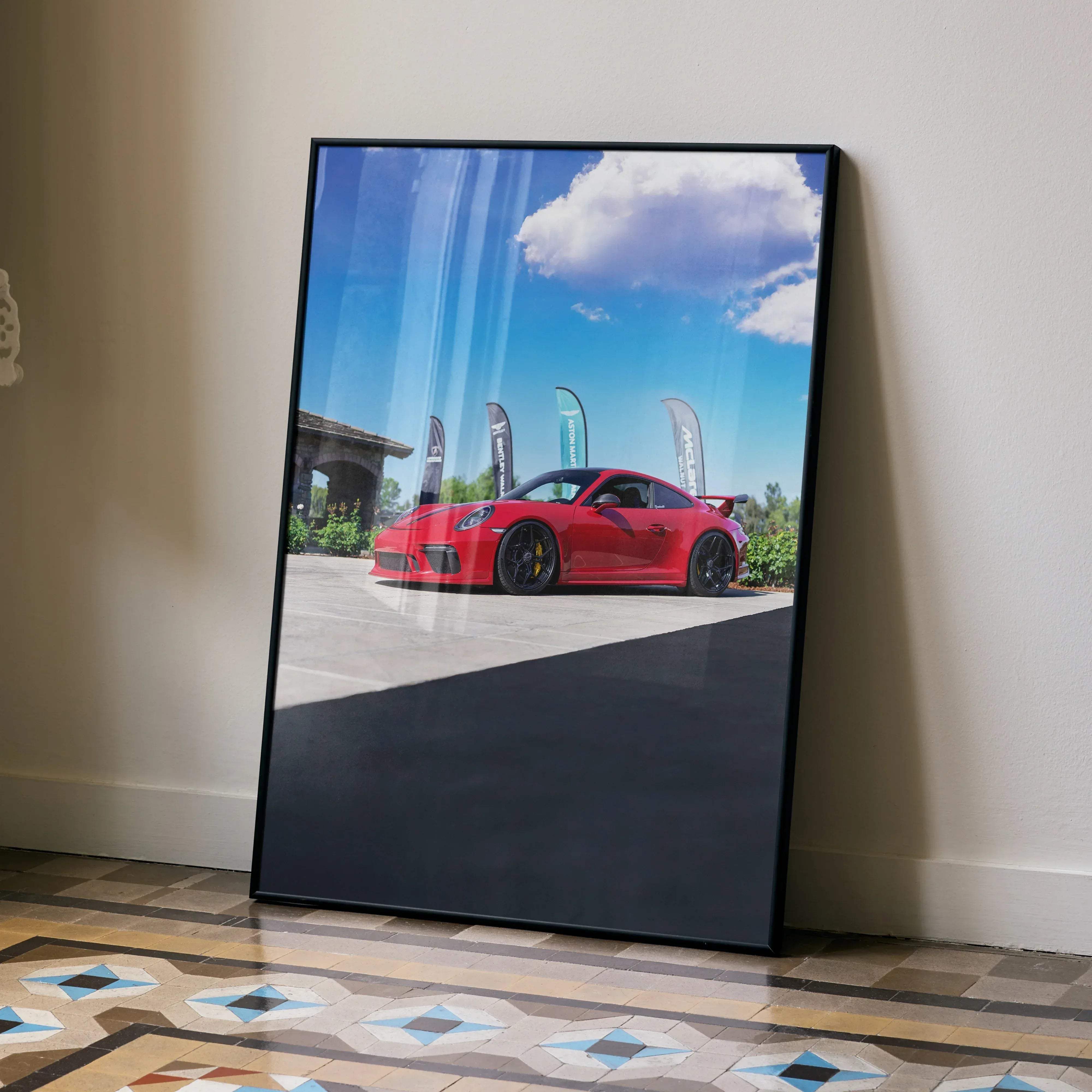 A framed photograph of a vibrant red Porsche 911 GT3 sports car under a bright blue sky with clouds poster