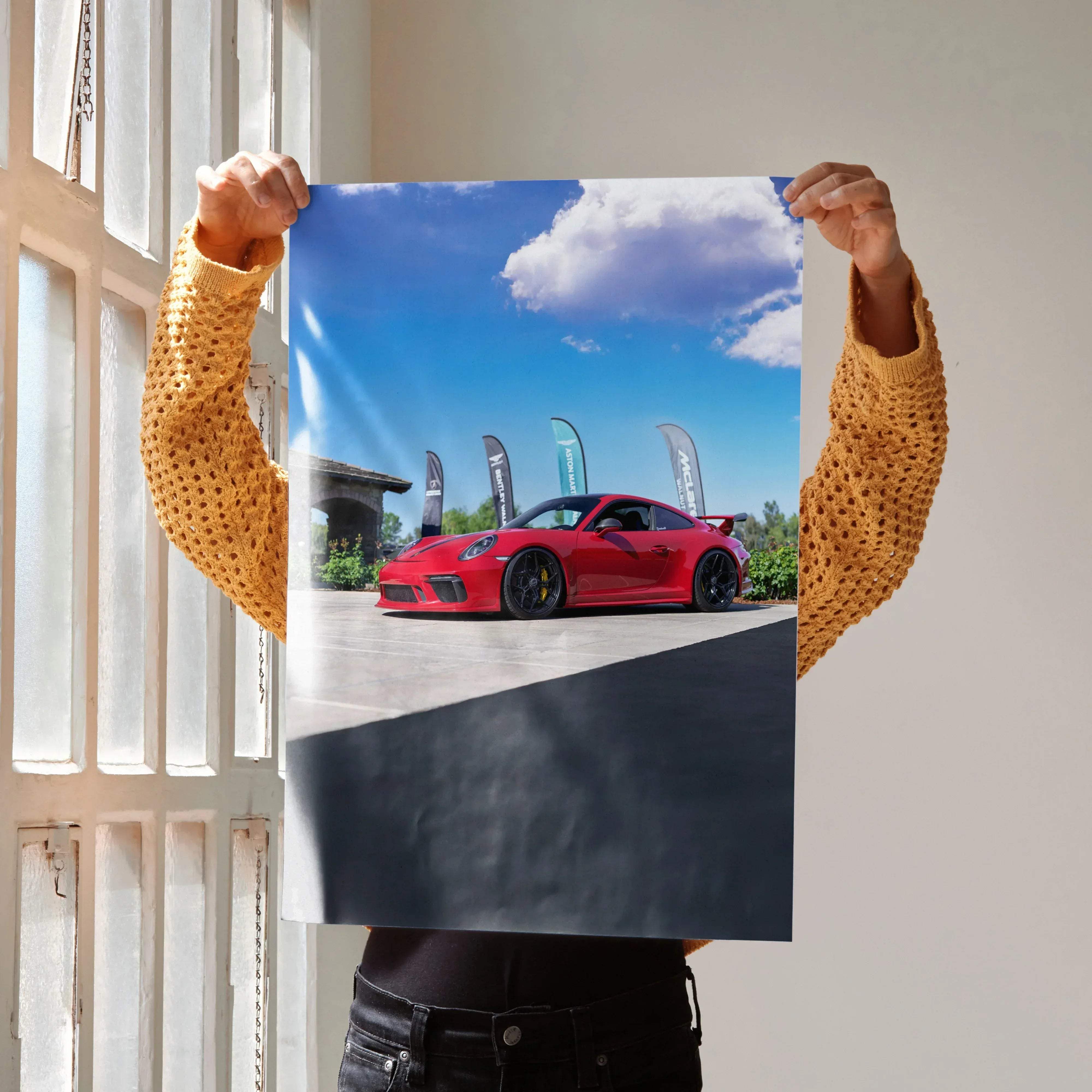 A vibrant red Porsche 911 GT3 sports car with black rims and rear spoiler under a bright blue sky outdoors