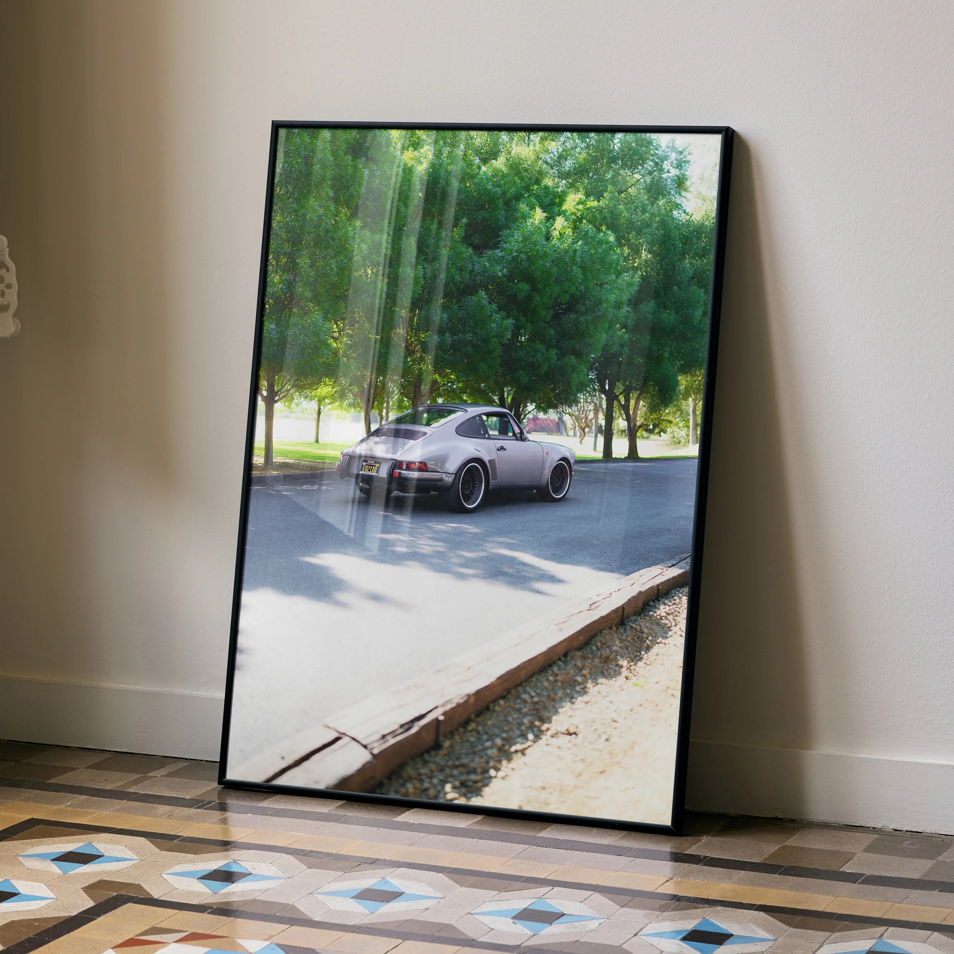 Porsche 911 classic car poster leaning against wall with outdoor park scene visible in reflective glass wall art.