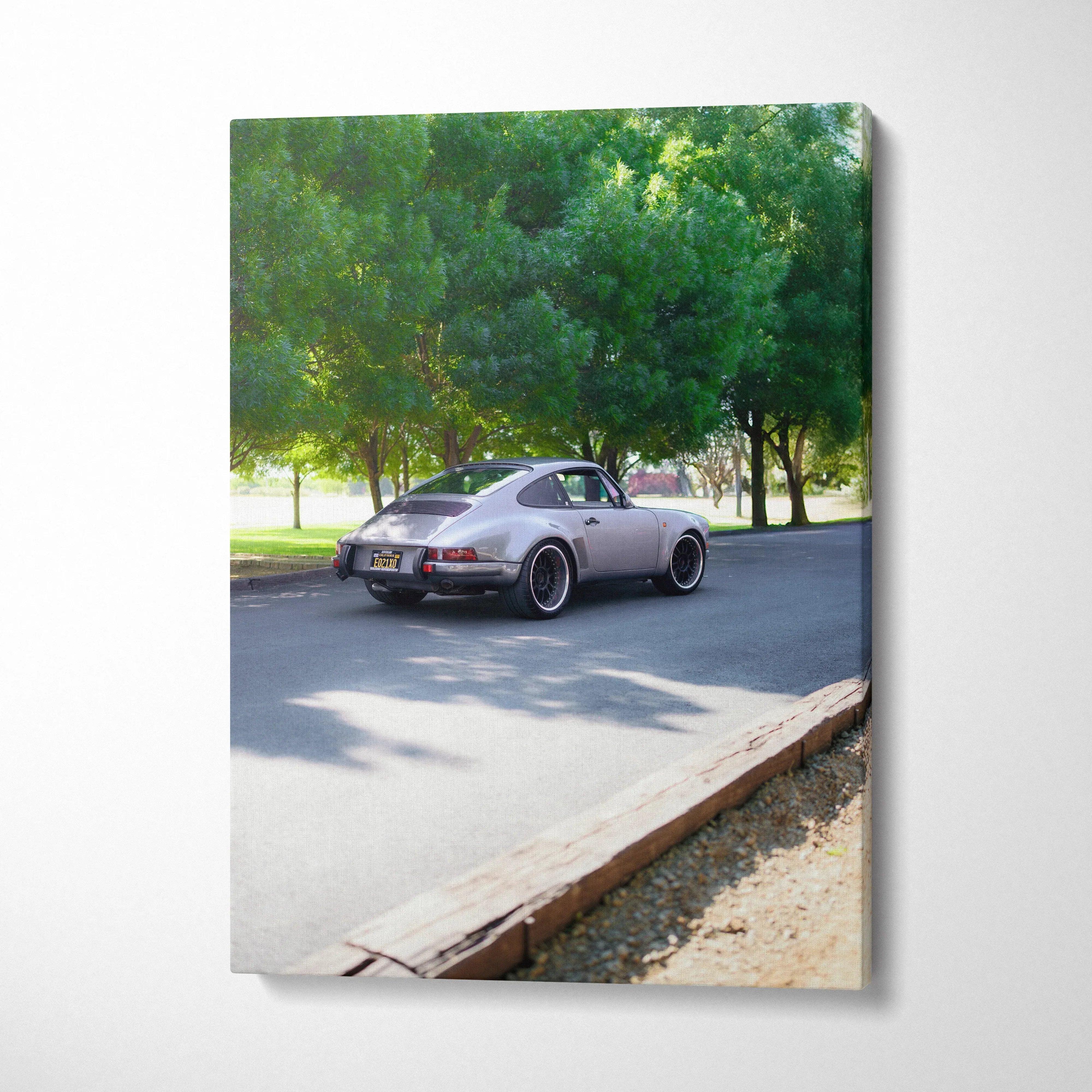 Vertical canvas wall art featuring a classic gray Porsche 911 parked on a sunlit road with green trees in the background.
