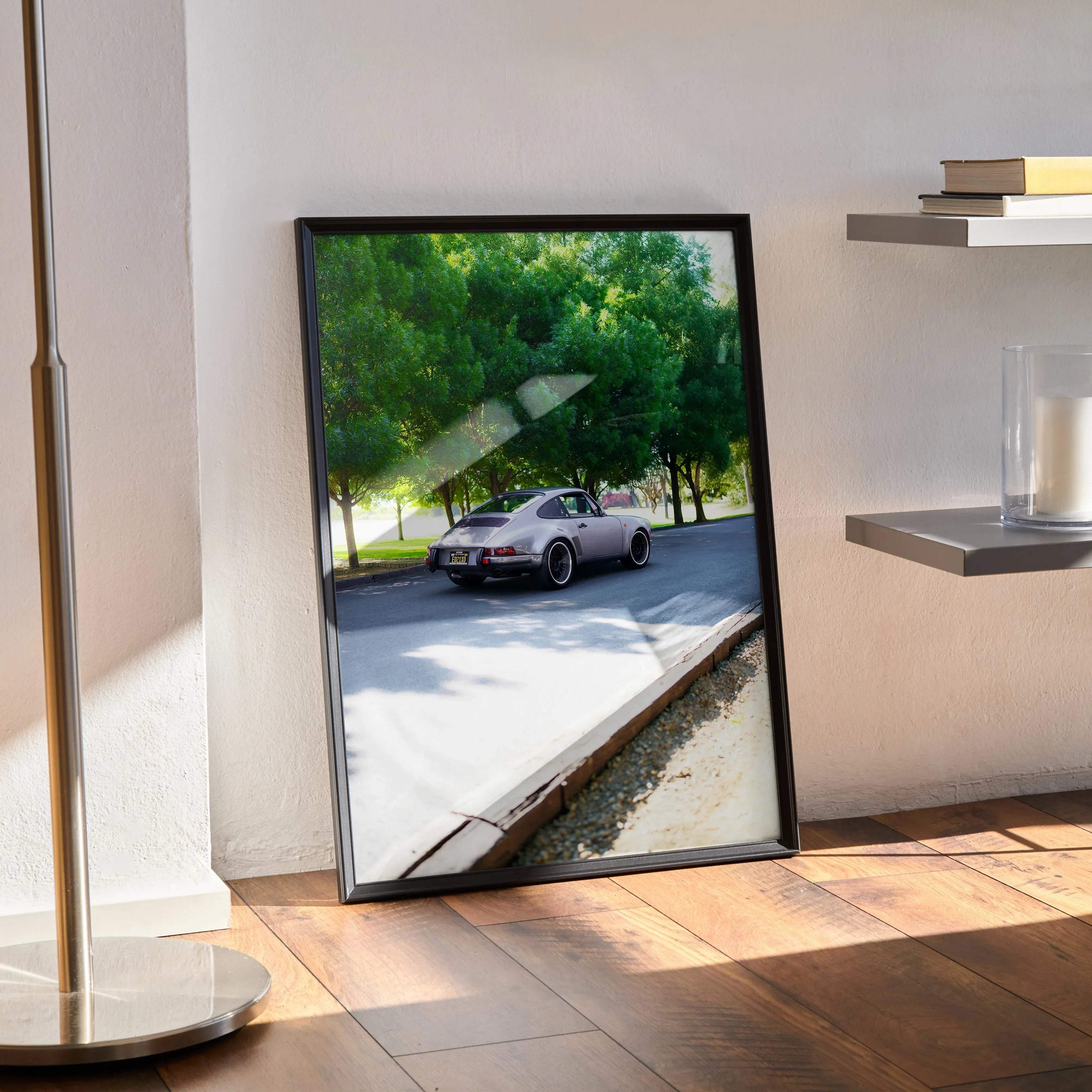 Black-framed art print featuring a silver porsche 911 driving on a tree-lined road in a classic car poster