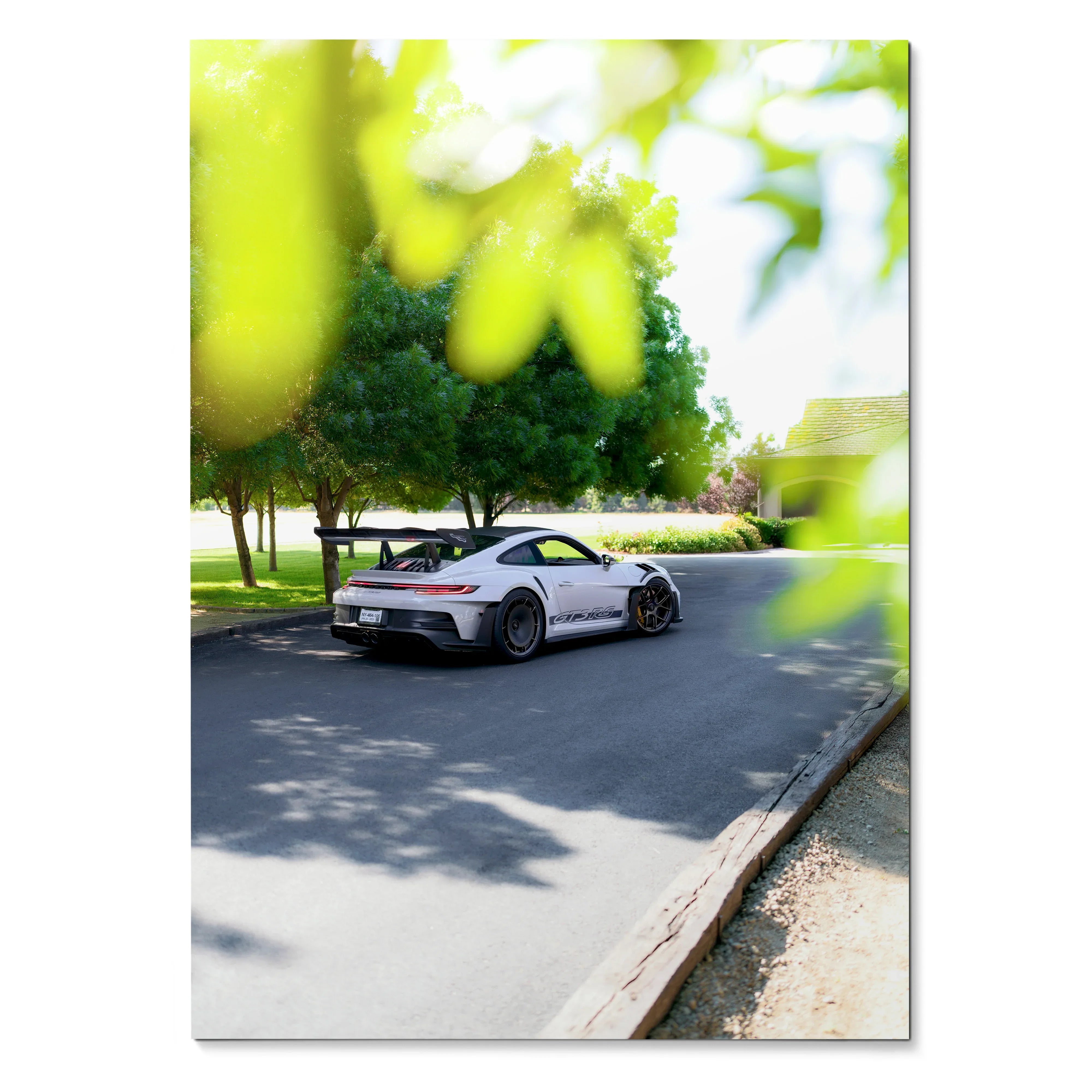 Porsche 911 GT3 RS driving on sunlit street surrounded by green trees poster wall art.