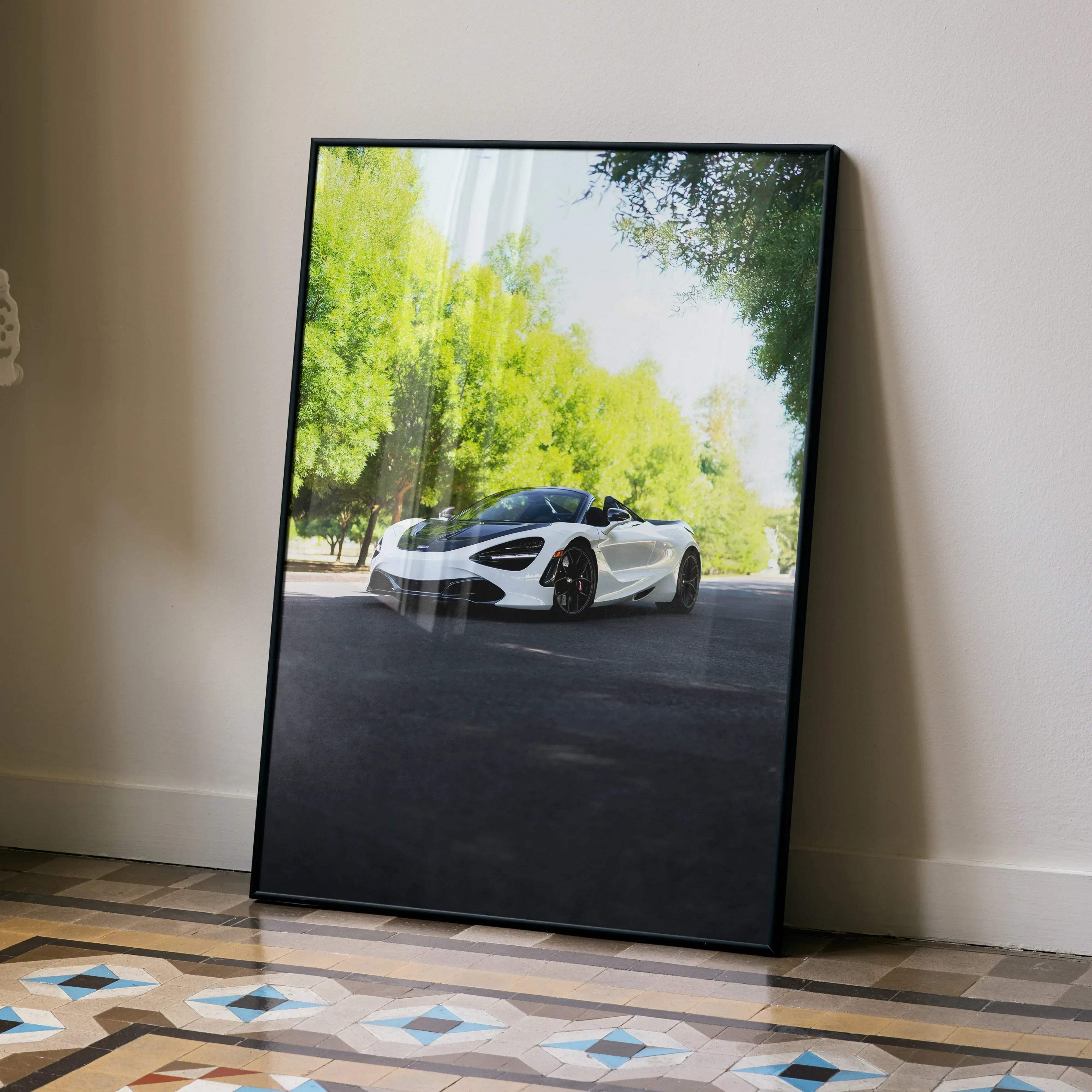 Black-framed poster of a white mclaren 720s spider sports car with black accents on a sunlit tree-lined road