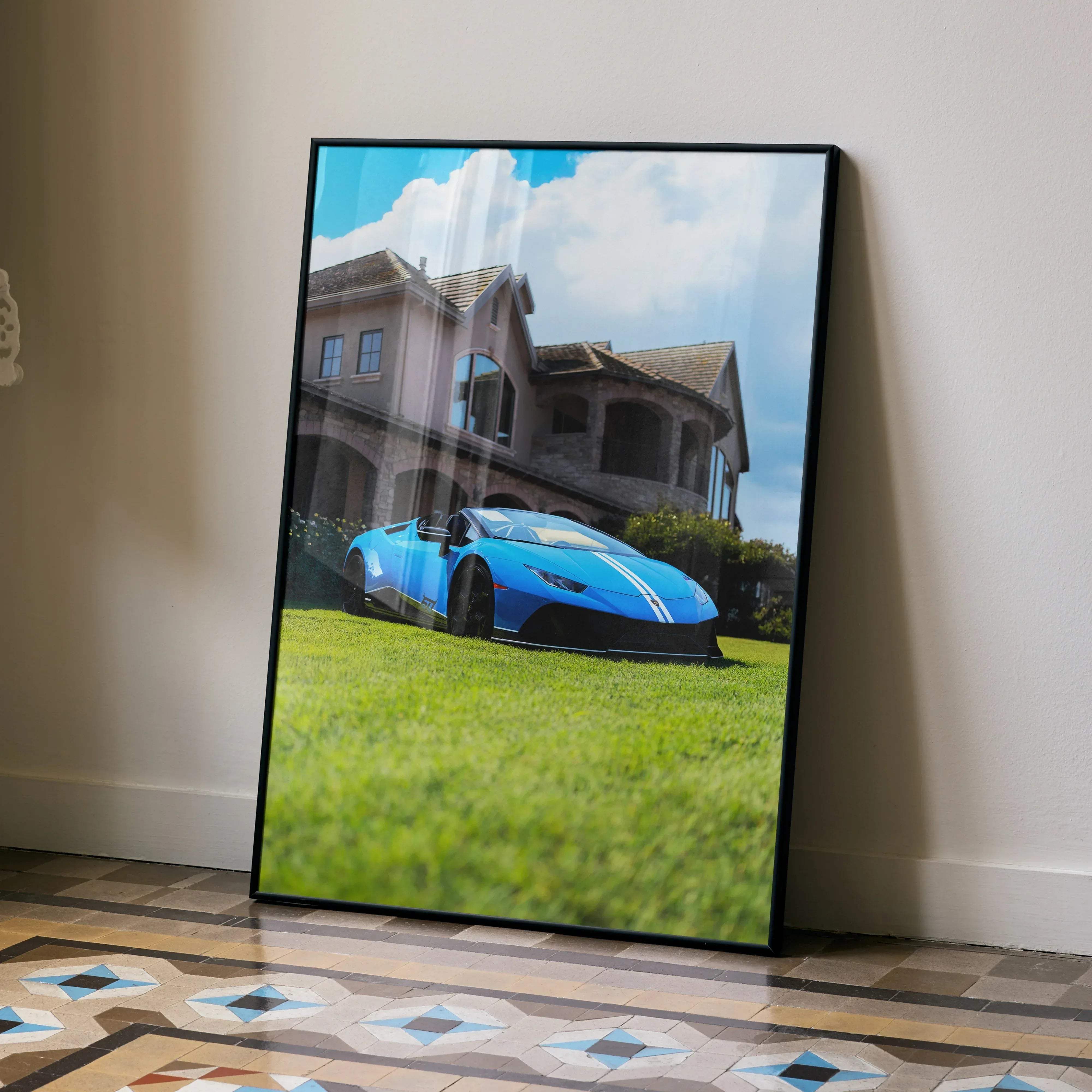 A framed print of a vibrant blue Lamborghini Huracan sports car parked on green grass in front of an elegant mansion