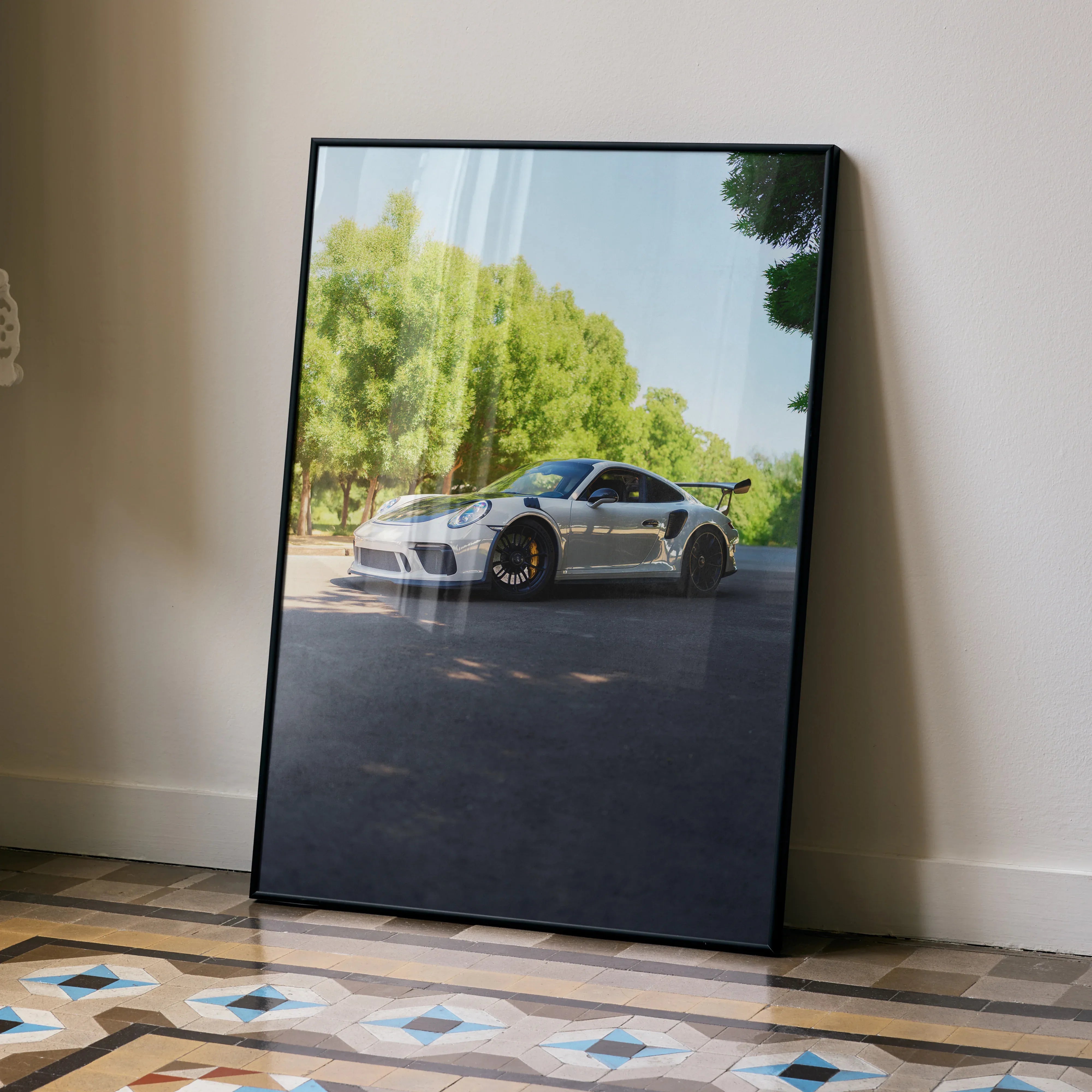 Porsche 911 GT3 poster with glossy finish leaning against a beige wall, showcasing sleek white sports car and greenery.