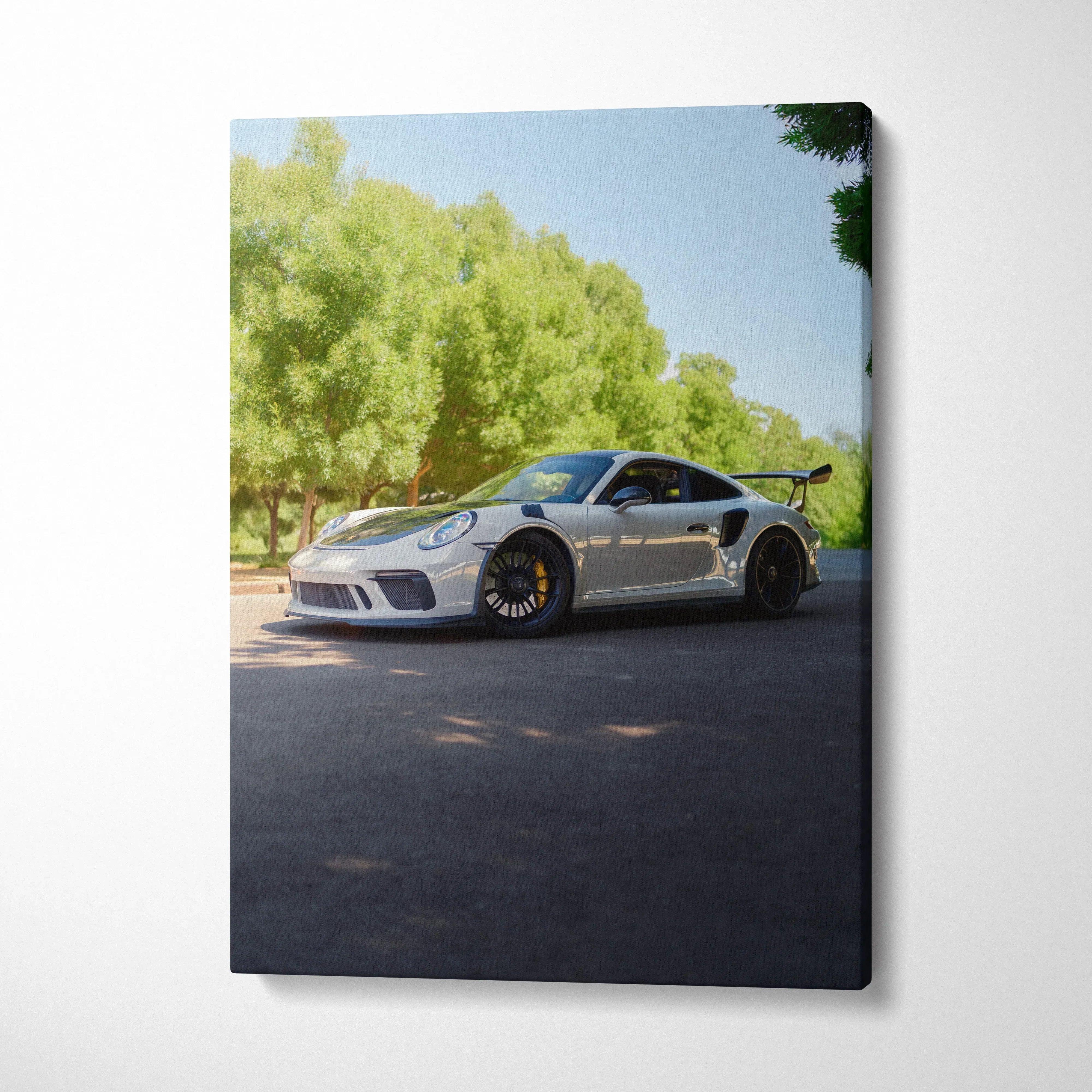 Vertical canvas art of a silver Porsche 911 GT3 parked on a sunlit road with green trees in the background.