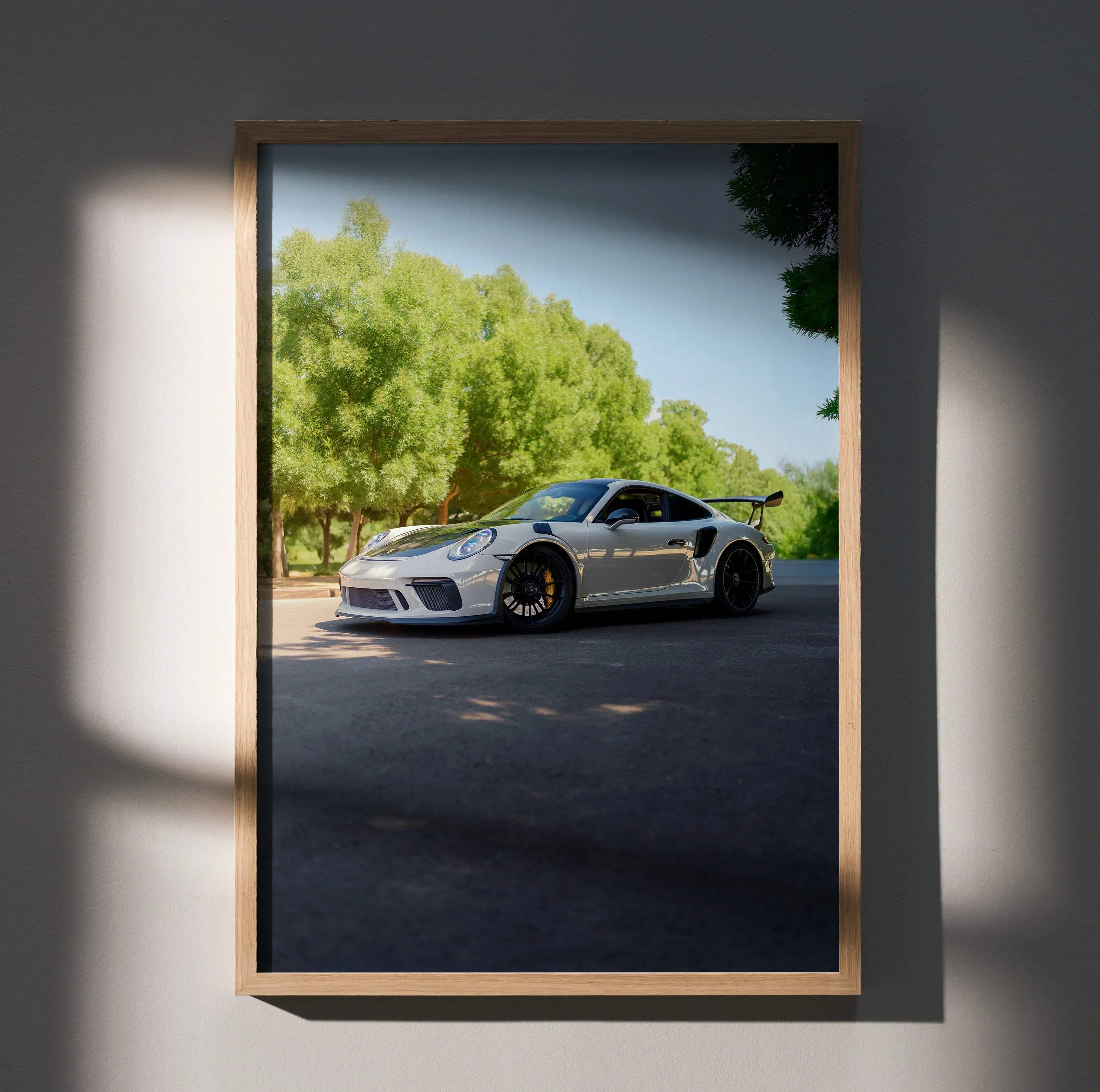 A framed photograph of a white Porsche 911 GT3 RS with black rims and orange brakes on asphalt road poster