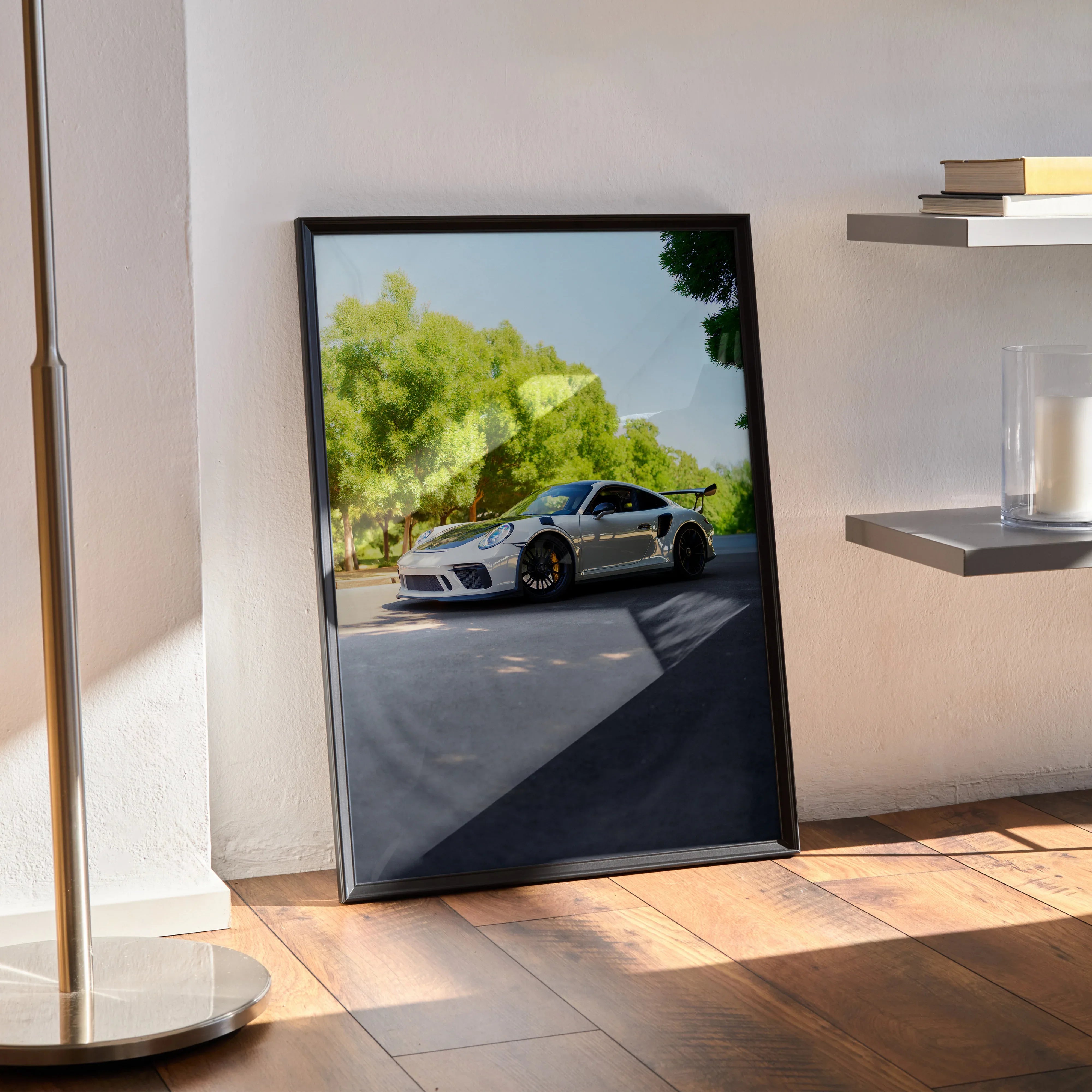 Porsche 911 GT3 poster with black frame leaning against wall, vibrant car and trees in background, modern wall art.