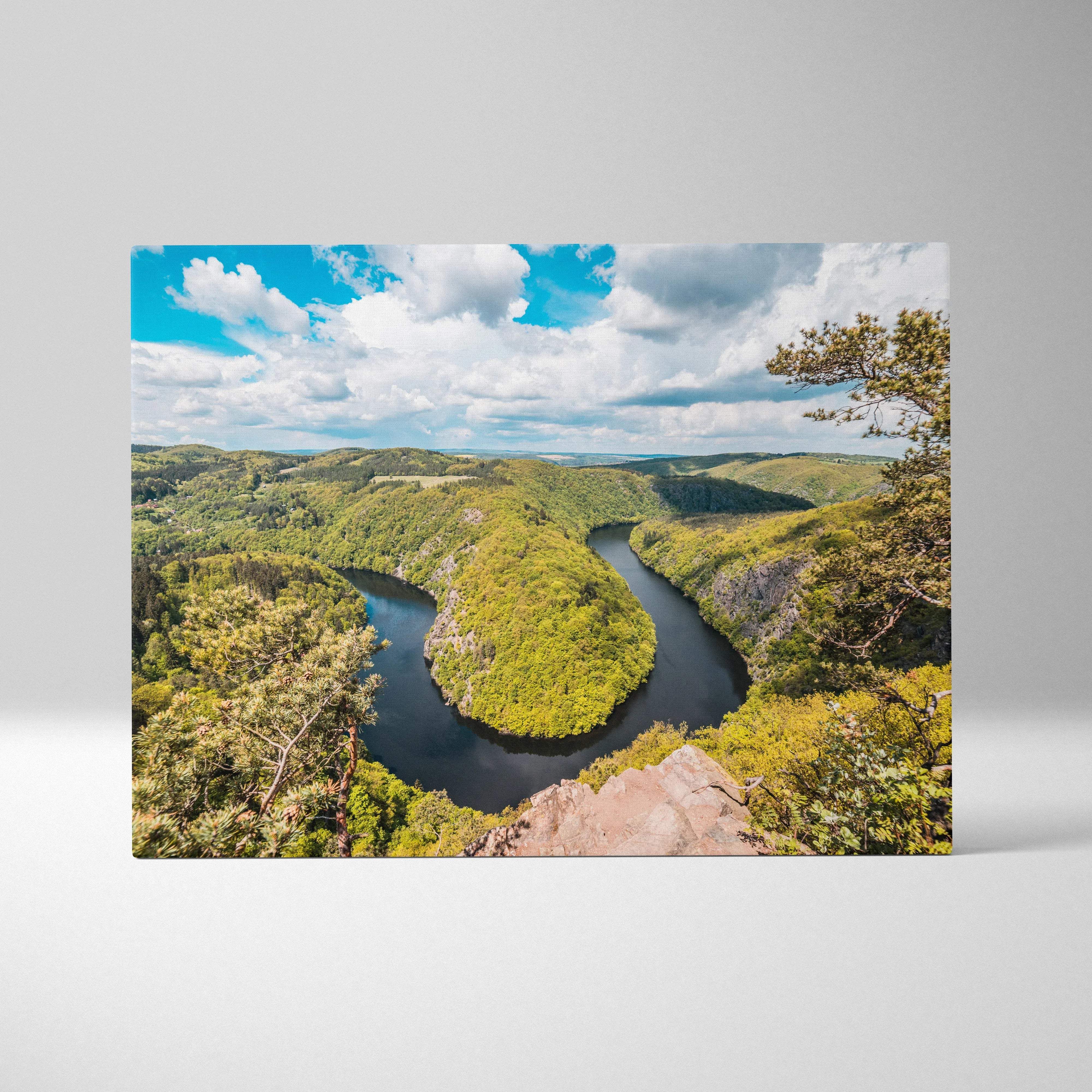 Canvas print of meandering river through lush green forest valleys under blue sky