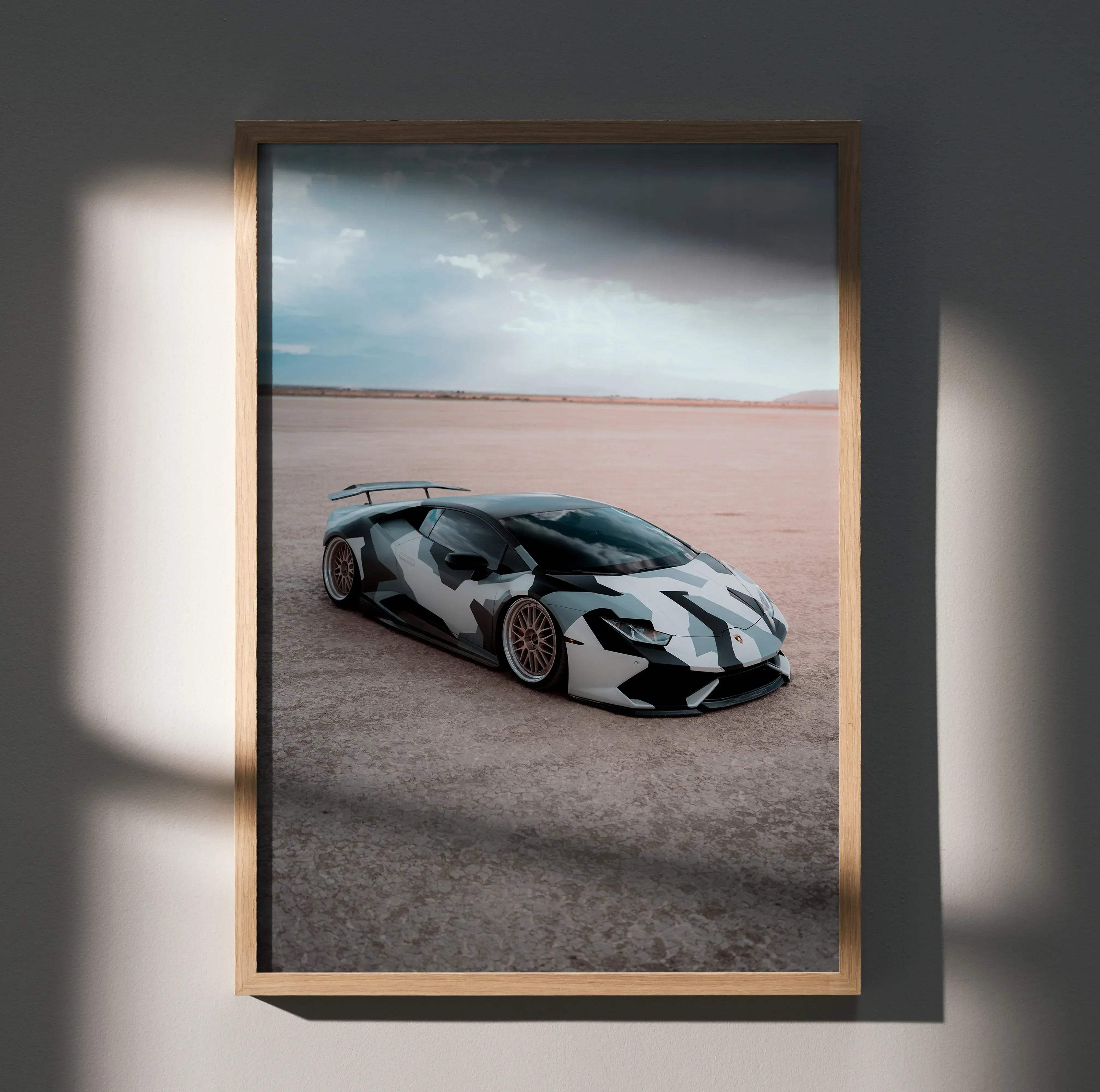A framed photograph of a Lamborghini Huracan with black and white camouflage paint in a light wood frame