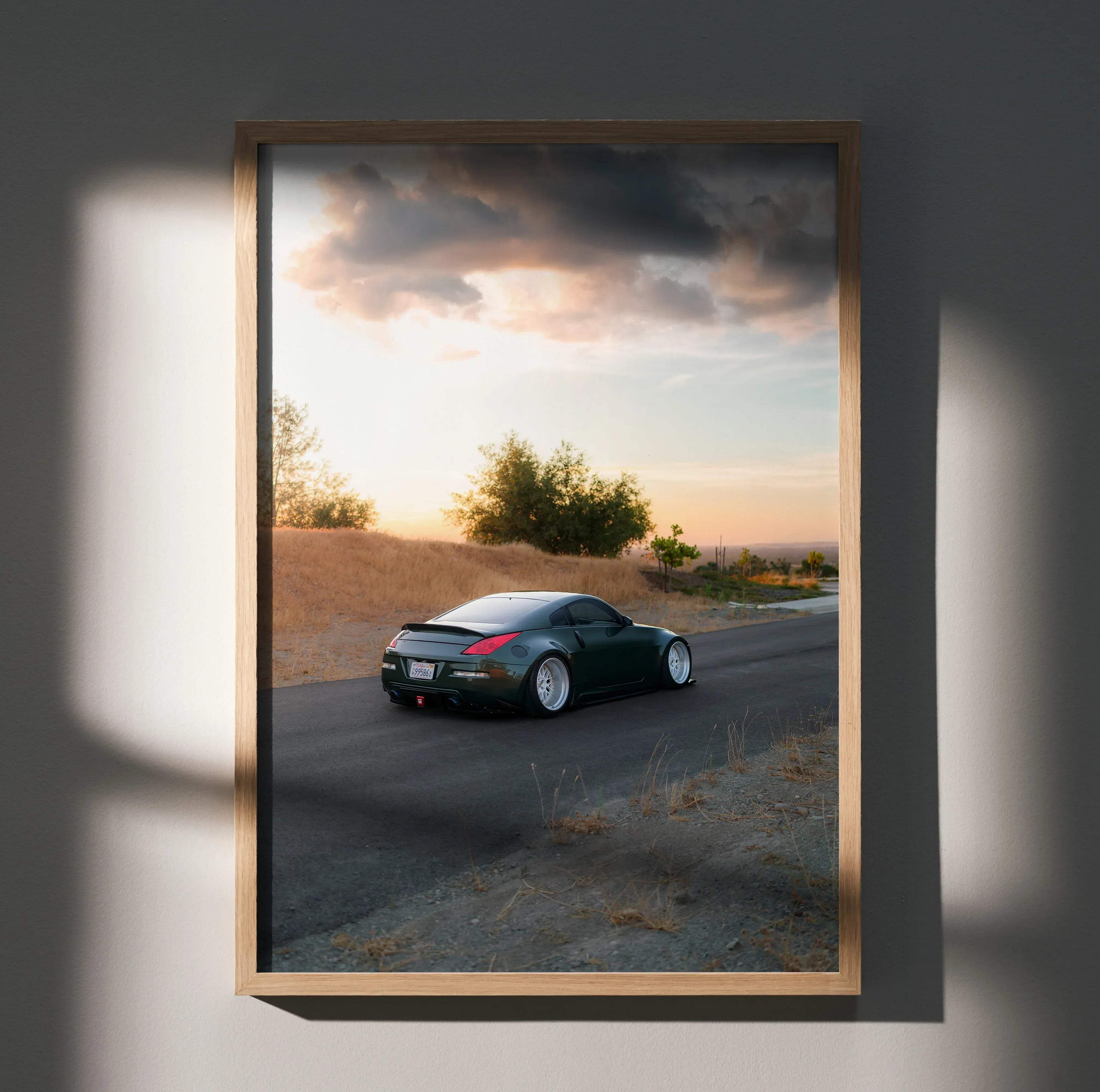 Dark green Nissan 350z sports car with white rims in motion on a winding road under dramatic sunset skies poster