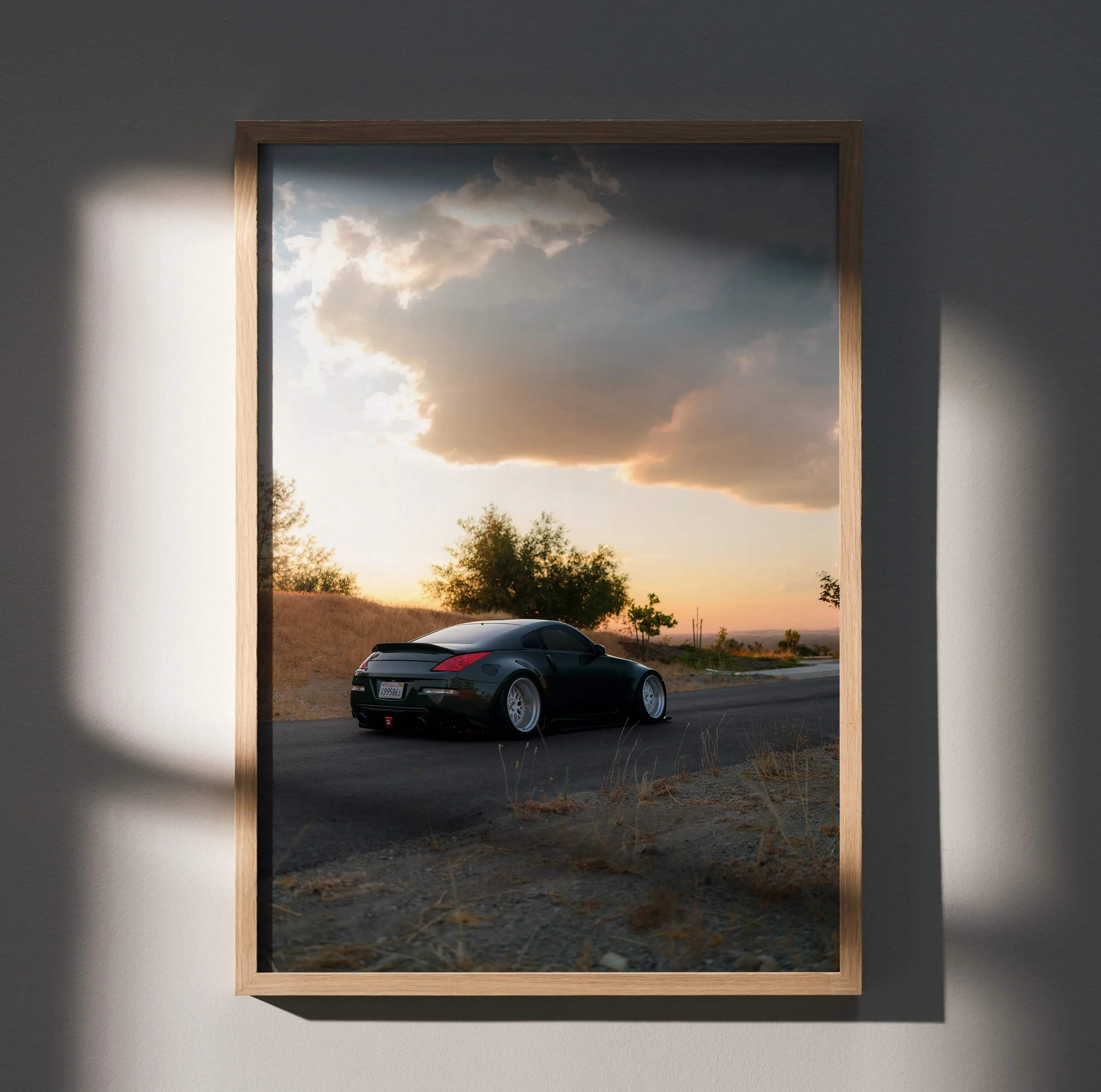 A framed photograph of a black nissan 350z sports car at sunset in a minimalist wooden frame for wall decor