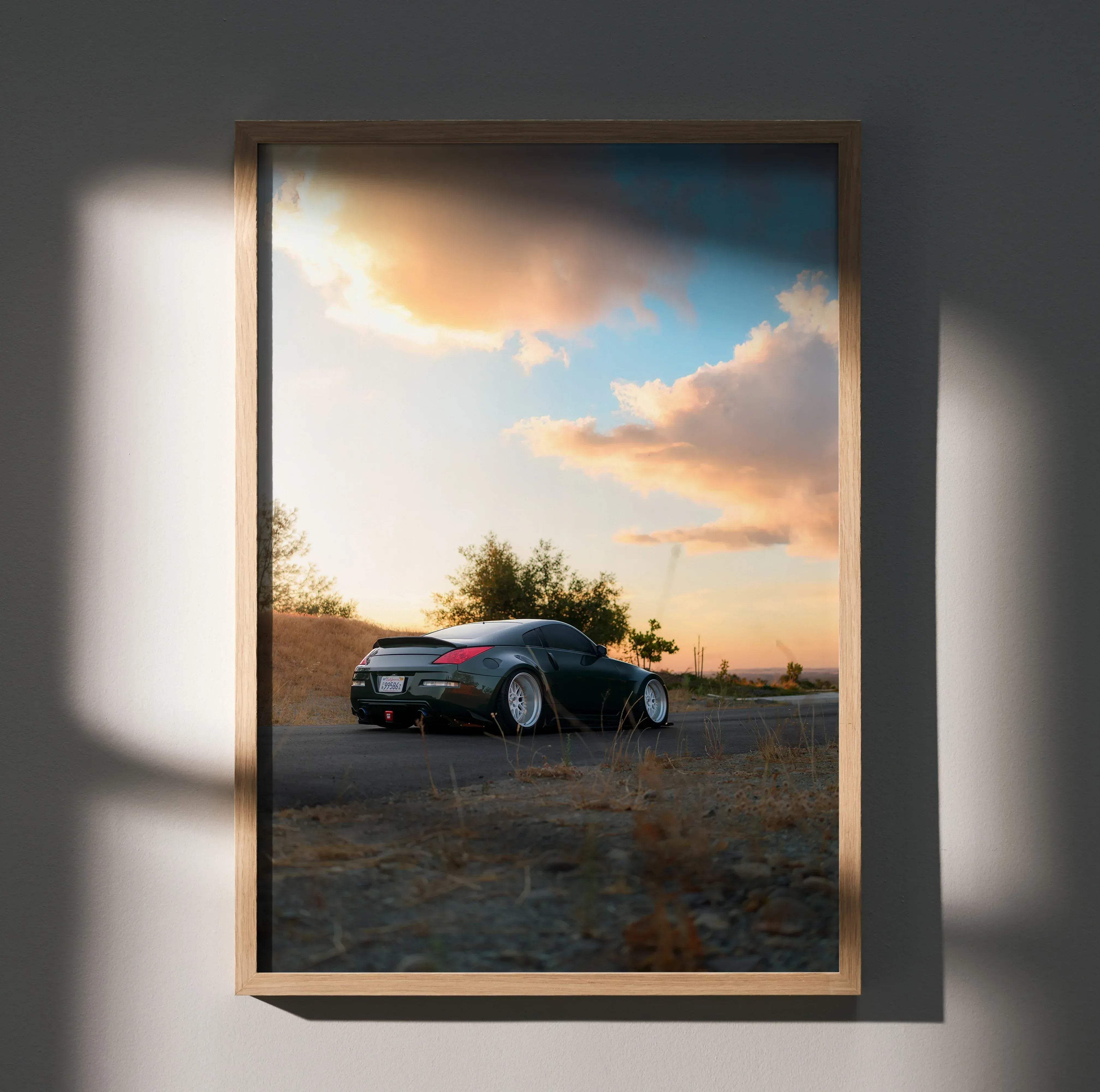 A framed high resolution poster of a dark green nissan 350z sports car on an open road at sunset in a wooden frame