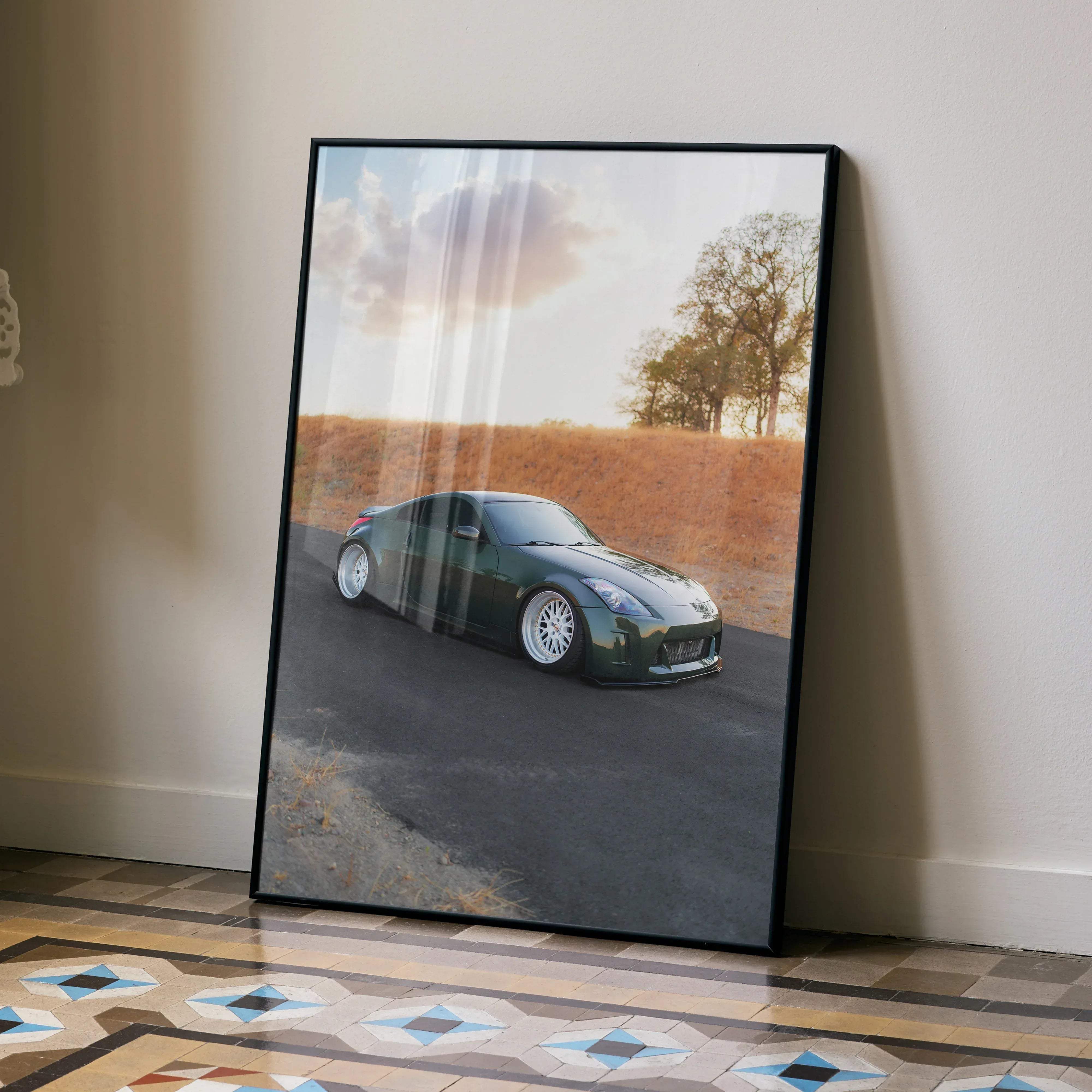 A framed high resolution poster of a dark green Nissan 350z sports car with white rims leaning against a wall