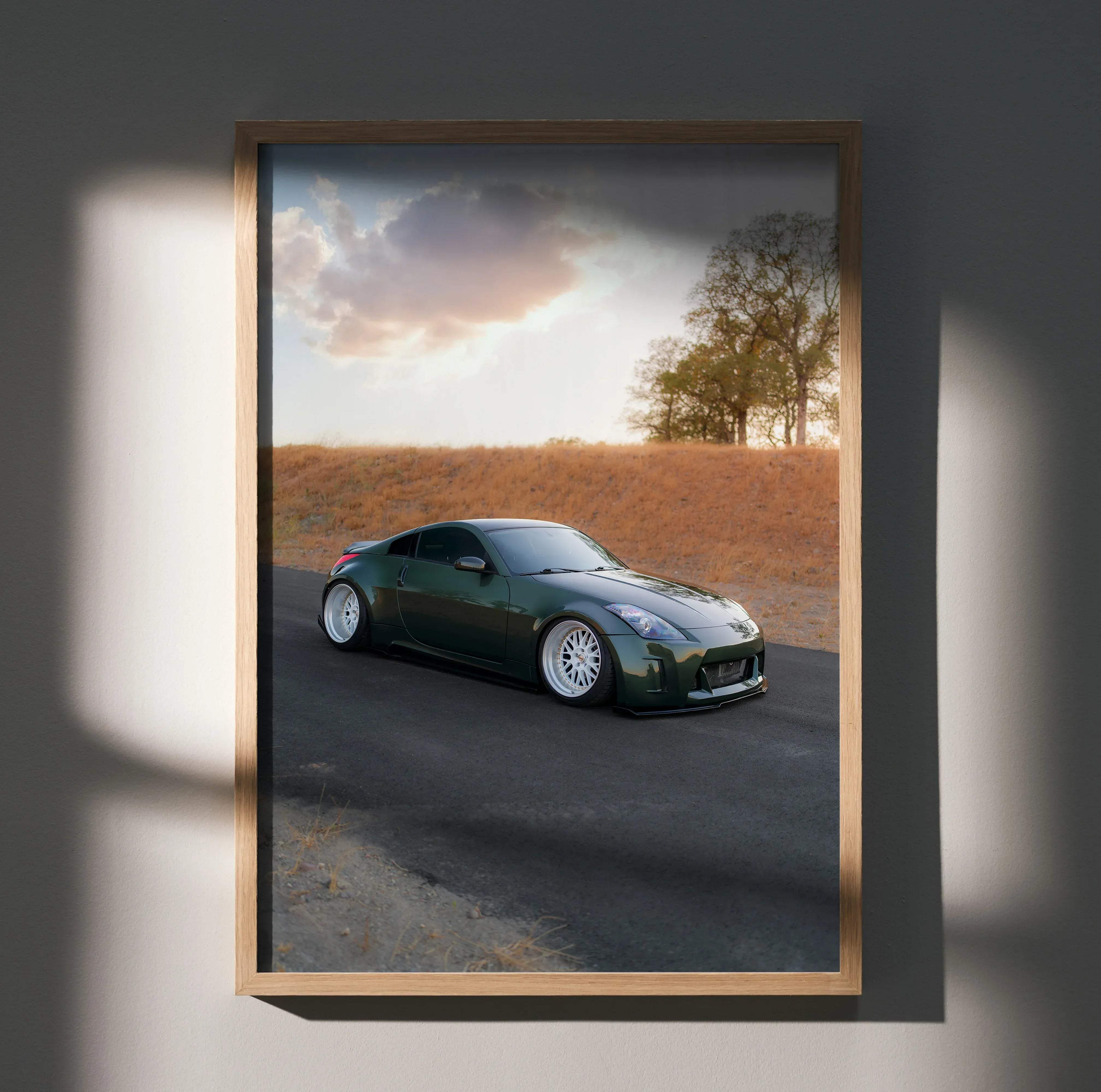 A framed photograph of a dark green Nissan 350z sports car with white rims on an asphalt road poster