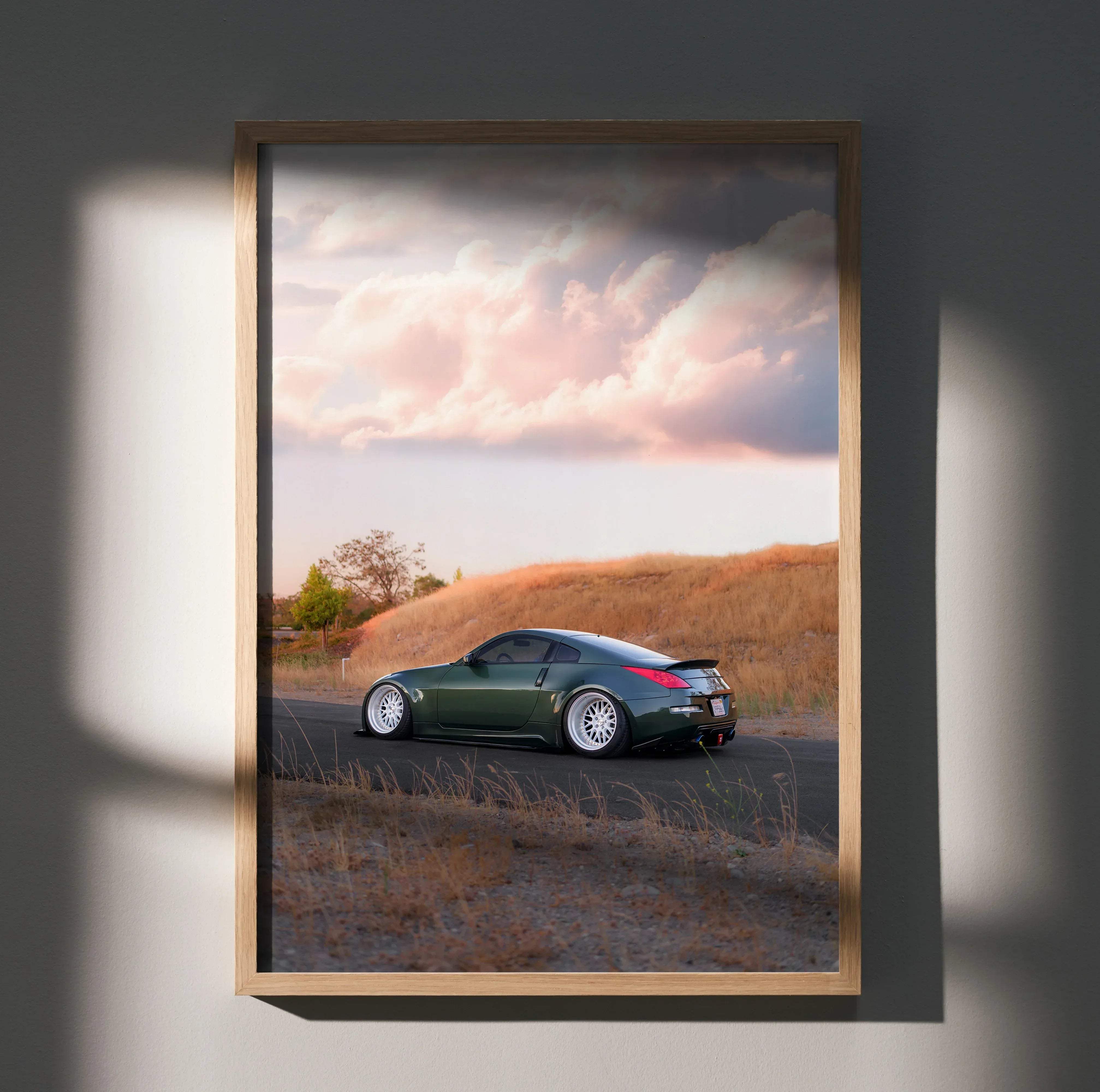 A framed photograph of a dark green Nissan 350z sports car with golden hills and pink clouds in the background