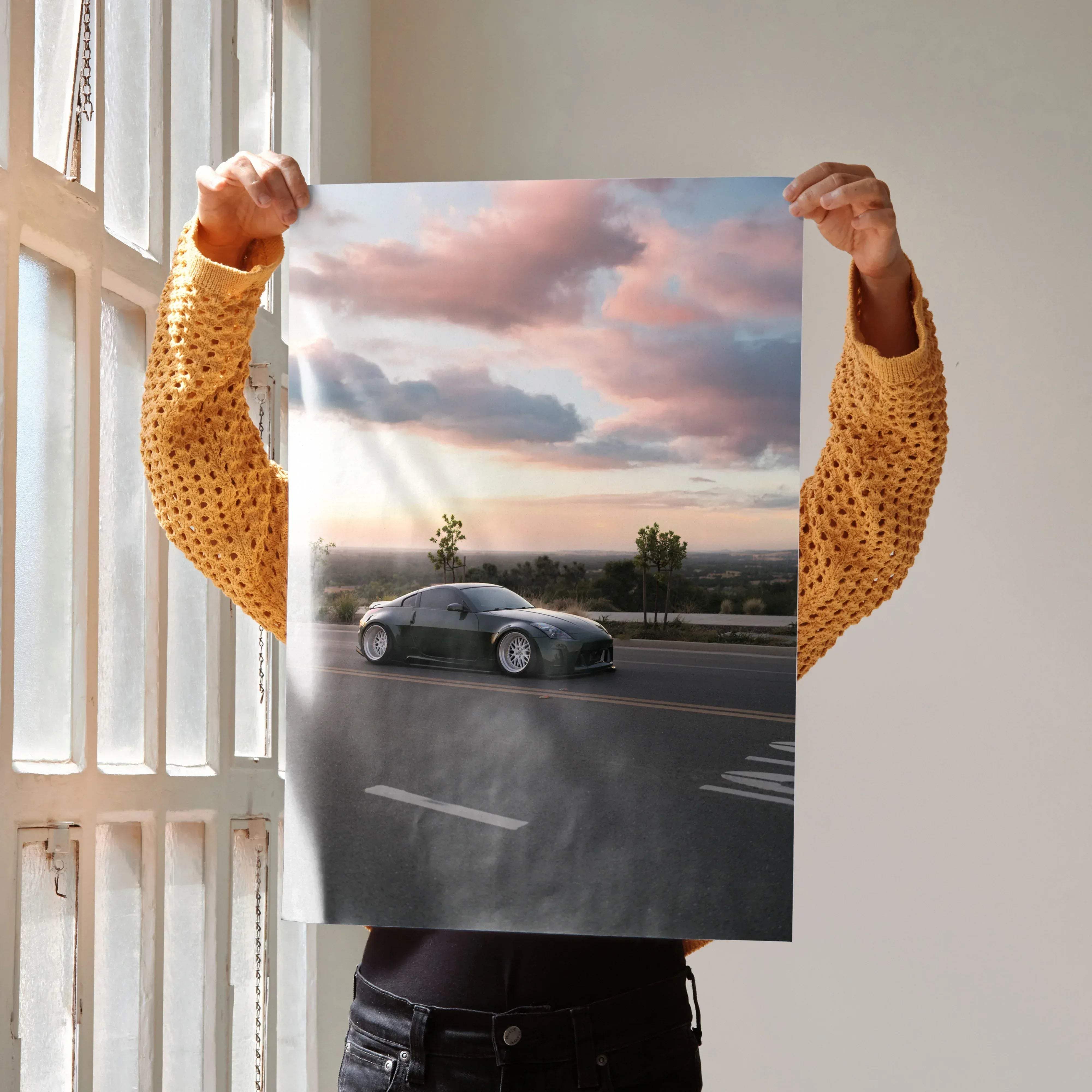 A sleek black Nissan 350z sports car poster in high resolution showing motion on an open road under a pink gray sky