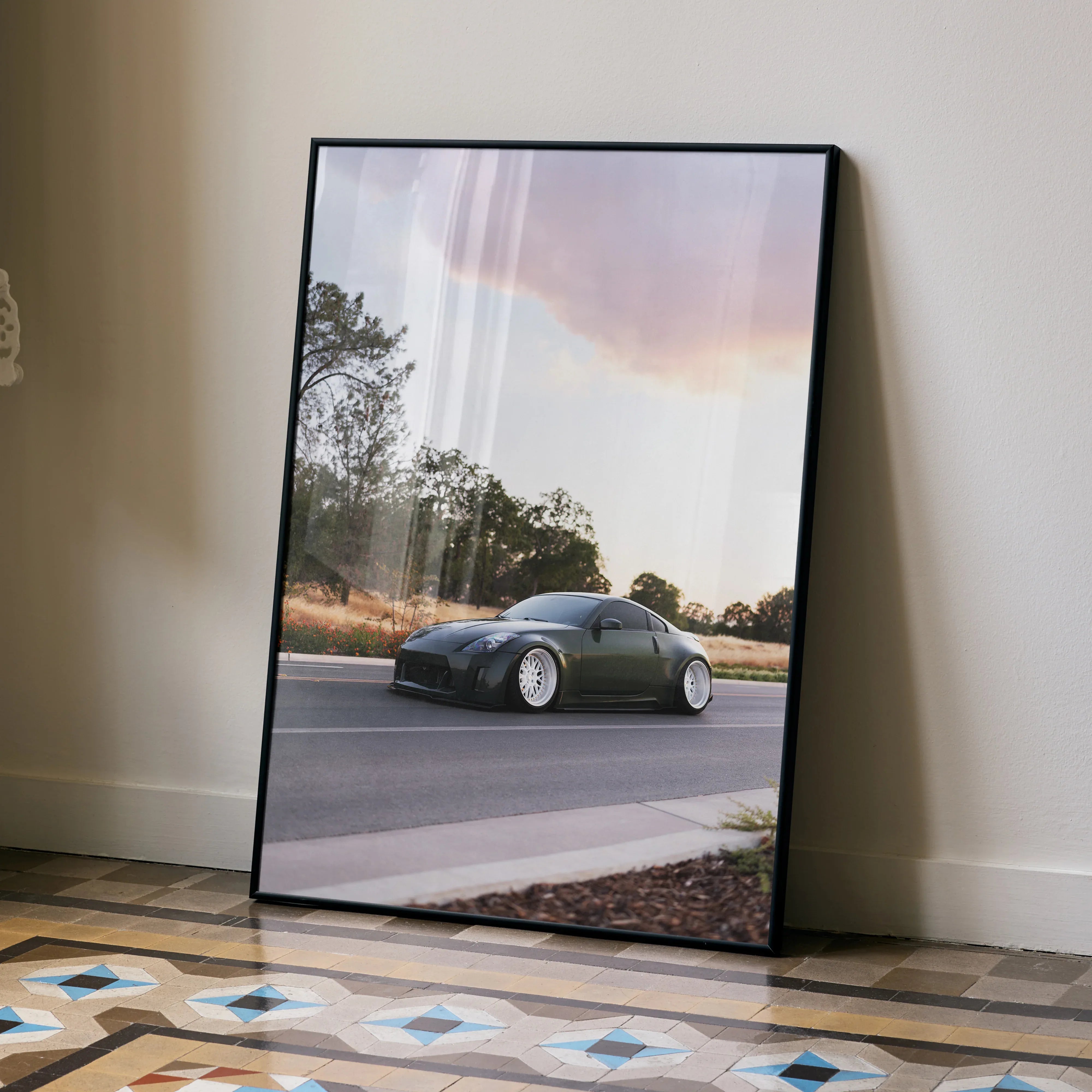 Nissan 350z sports car driving on road against sunset sky poster wall art in black frame.