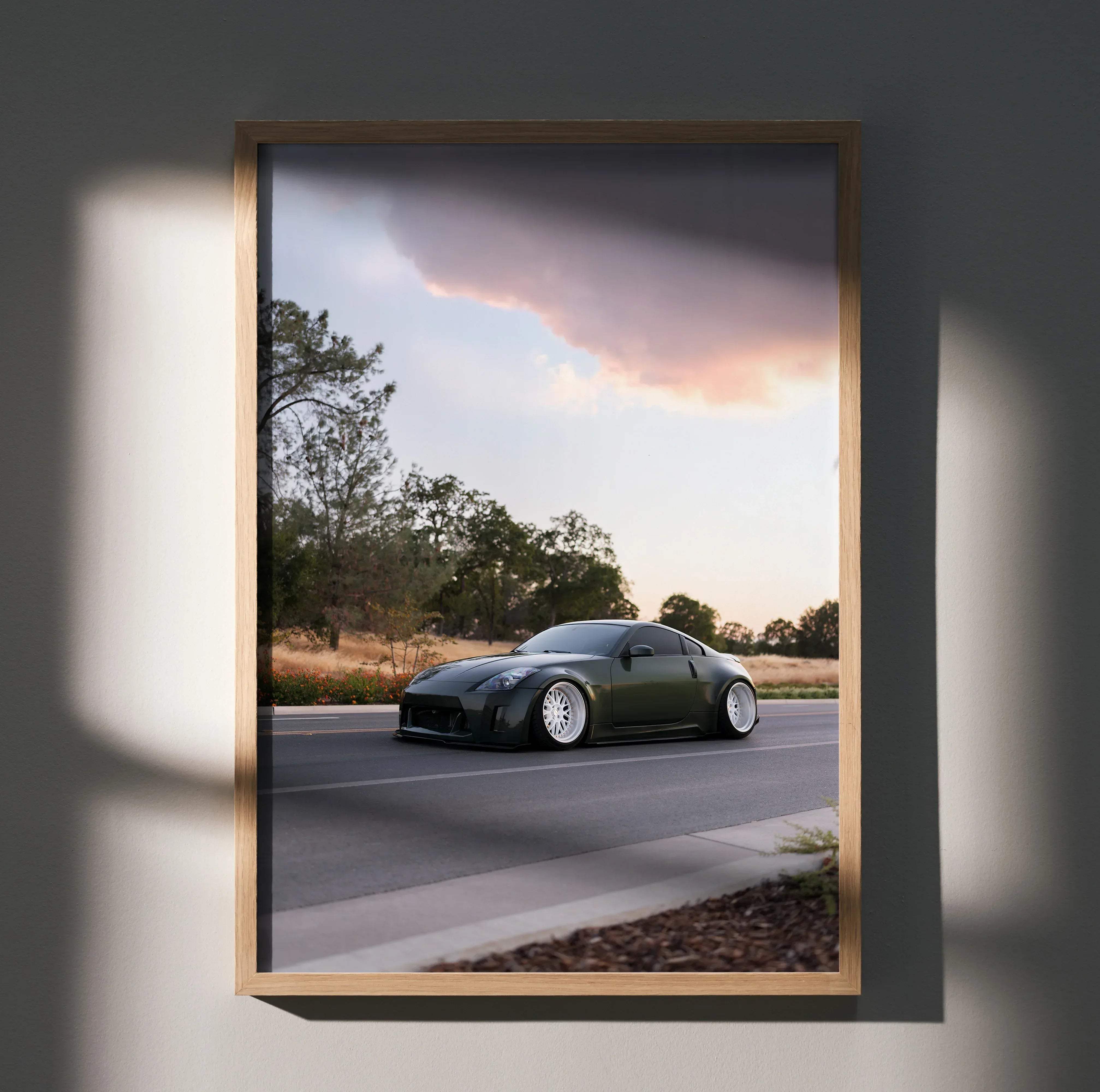 A framed photograph of a dark green Nissan 350z sports car with white rims on a road under a dramatic sky poster
