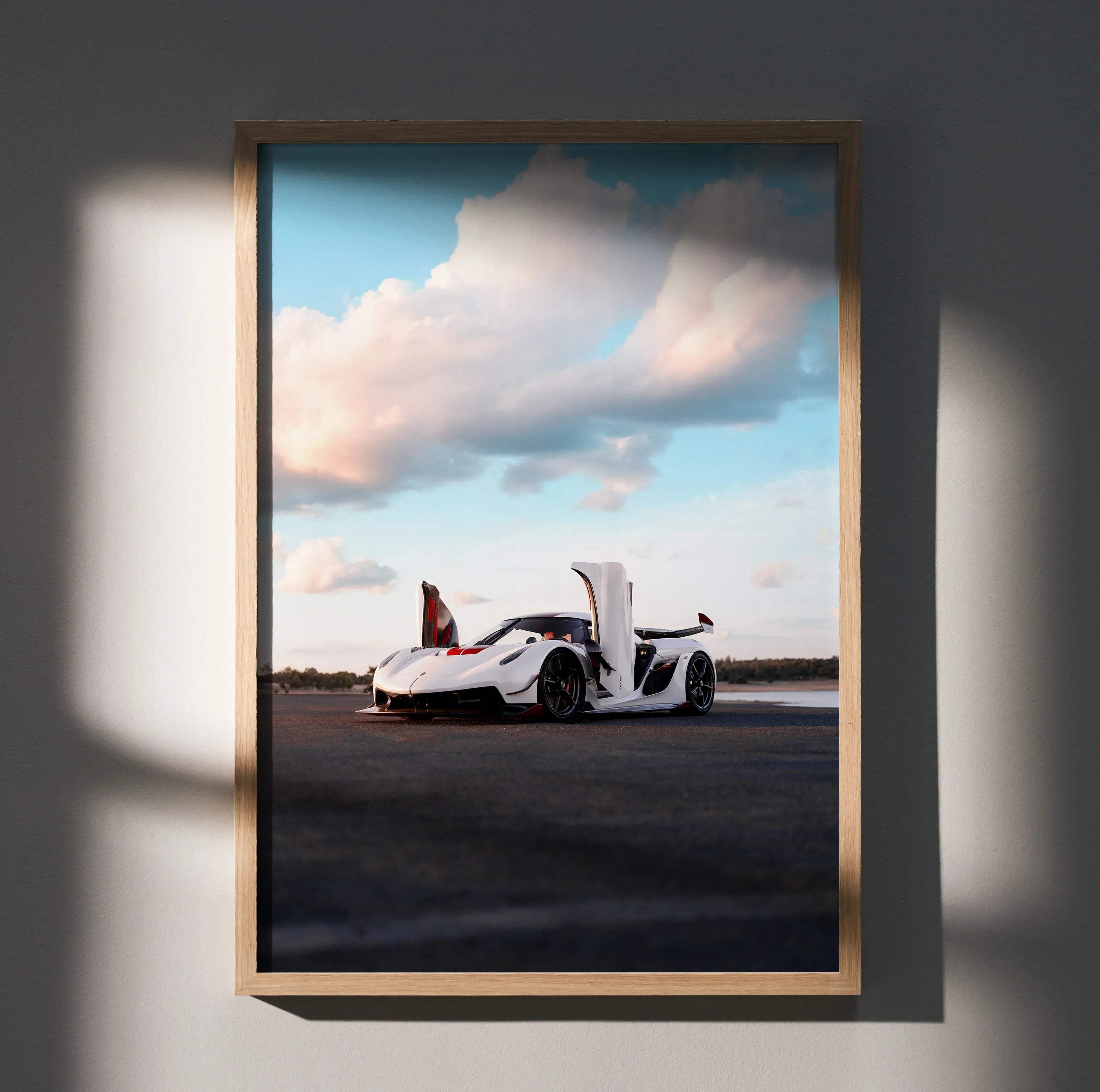 A framed photograph poster of a white Koenigsegg Jesko hypercar with open doors against a cloudy sky background