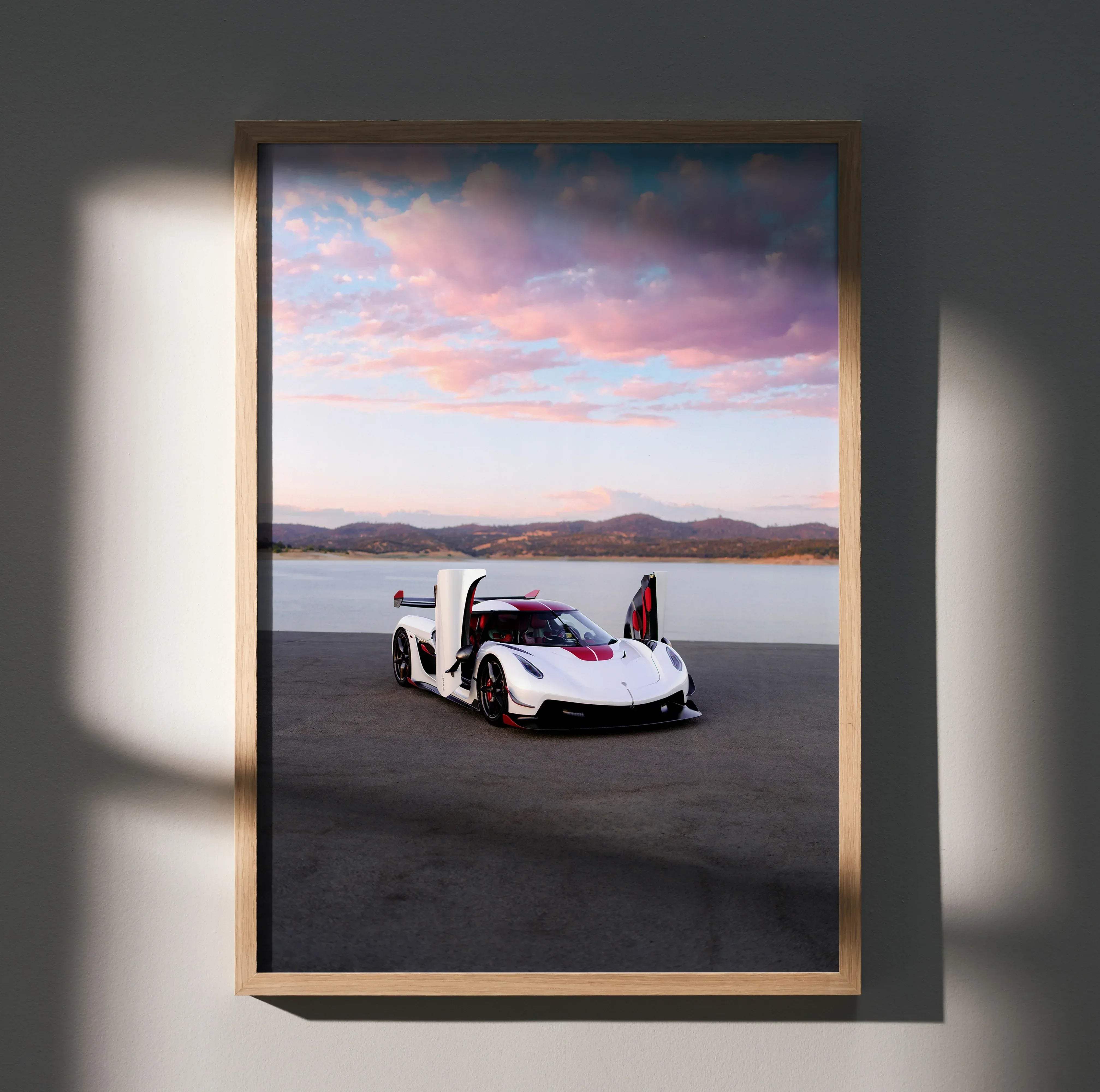 A framed high resolution koenigsegg jesko car poster of a white and red hypercar with open doors by a lakeside