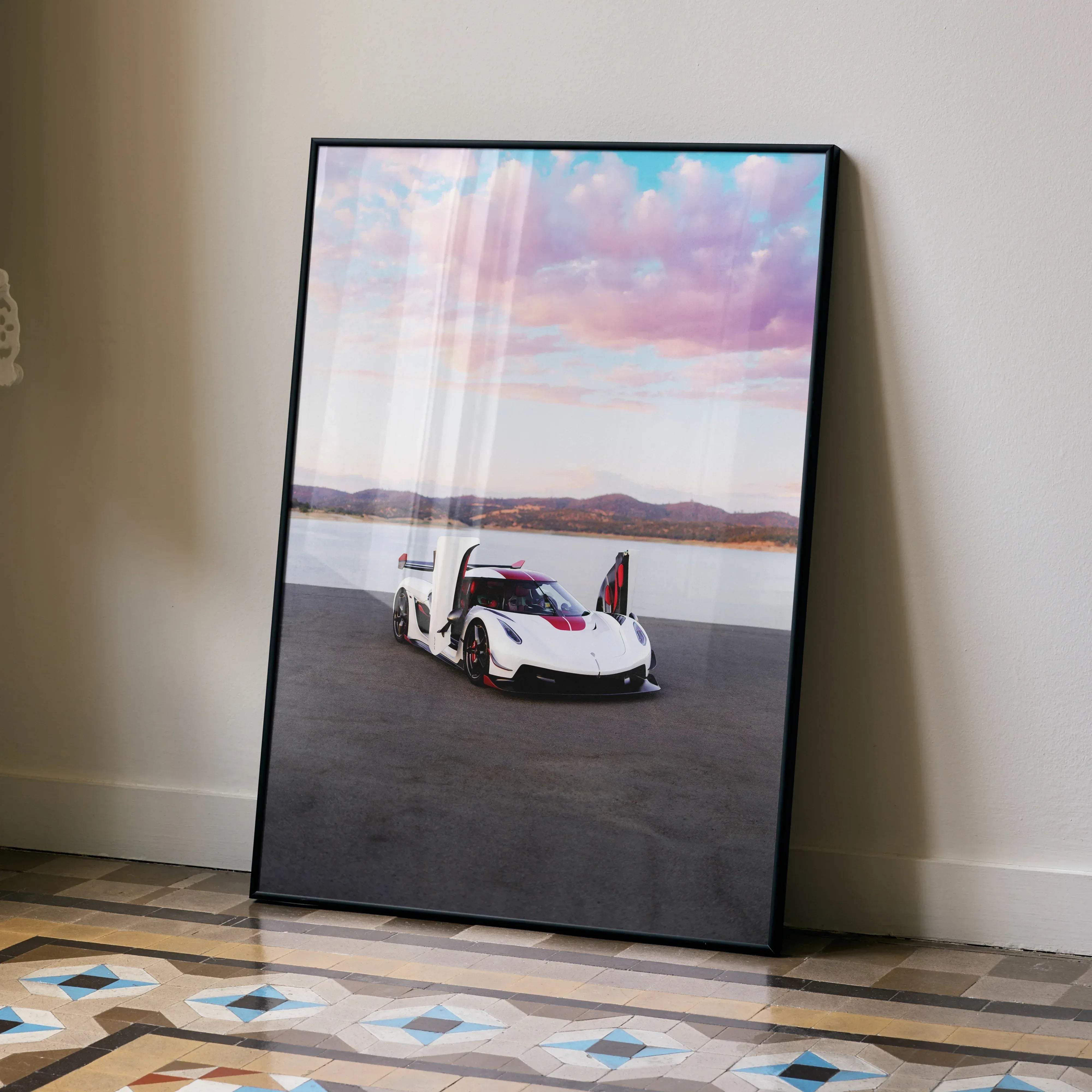 A framed poster of a white and red Koenigsegg Jesko hypercar with open doors against water and mountain scenery
