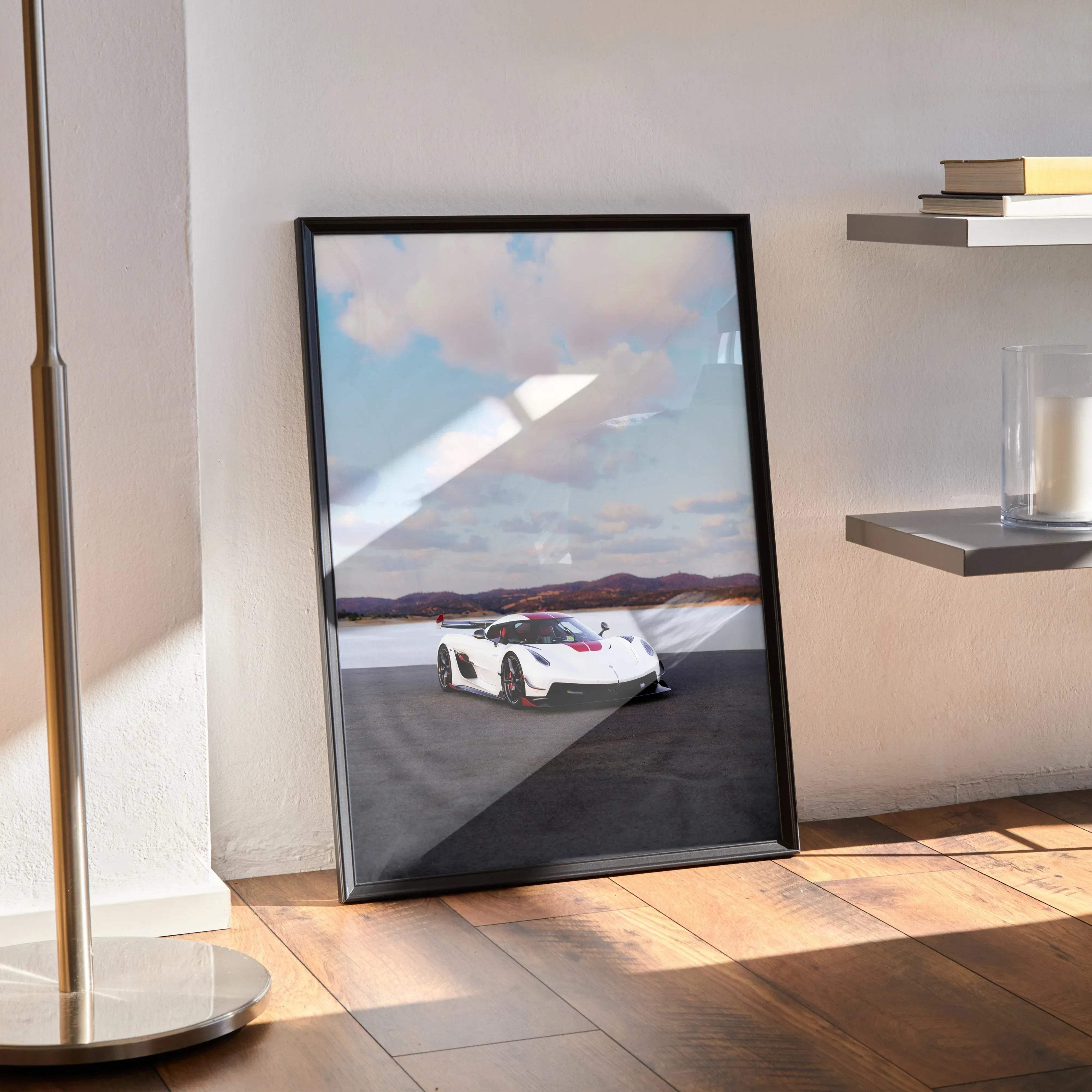 Black-framed poster of white koenigsegg jesko hypercar with red accents speeding on asphalt track under cloudy sky