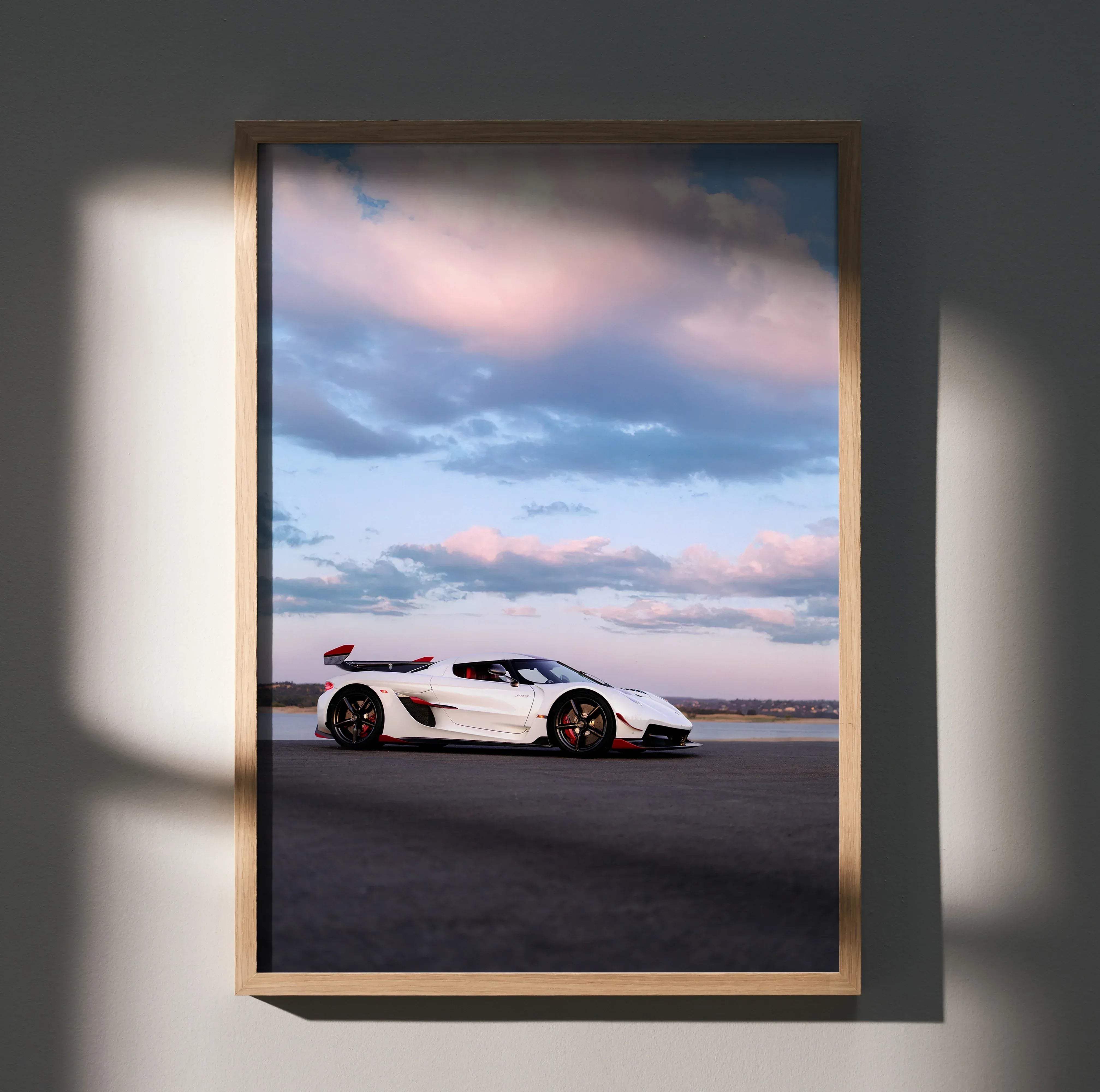 A framed poster of a white koenigsegg jesko hypercar with red accents and black wheels against a dramatic sky