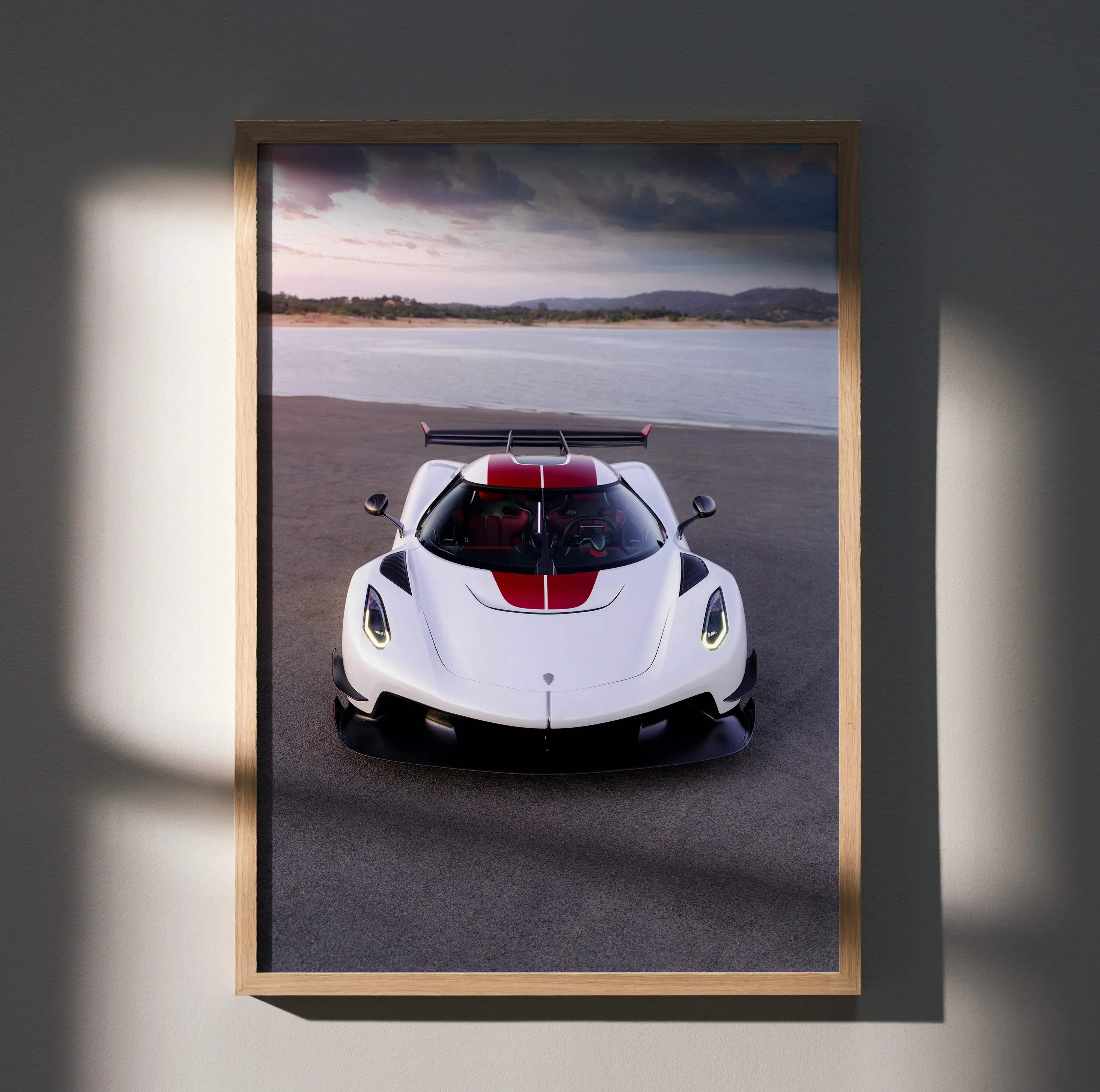 A framed photograph of a white and red koenigsegg jesko hypercar with black accents in a light wood frame
