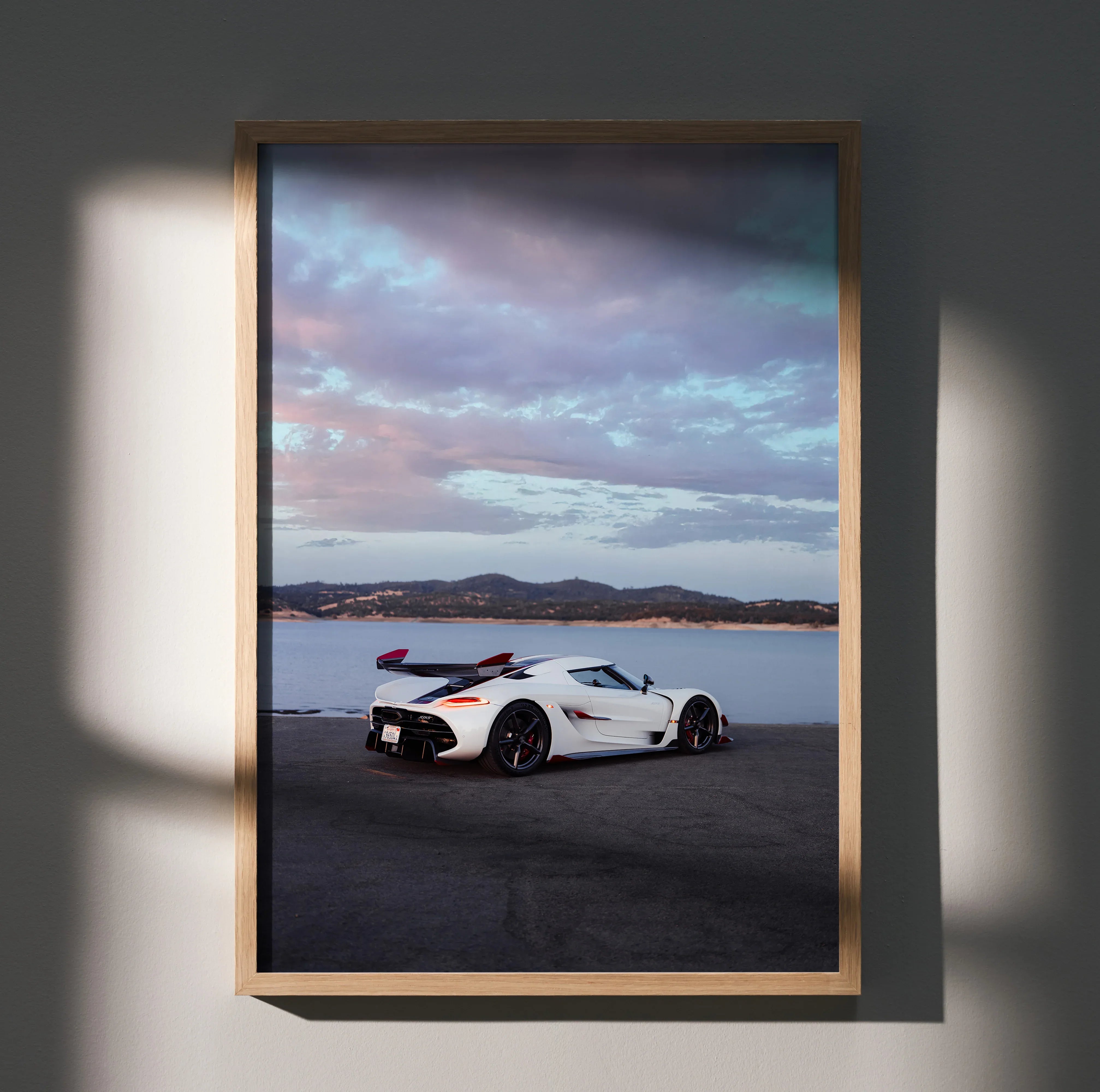 Koenigsegg Jesko white sports car on coastal road at sunset poster wall art in wooden frame.