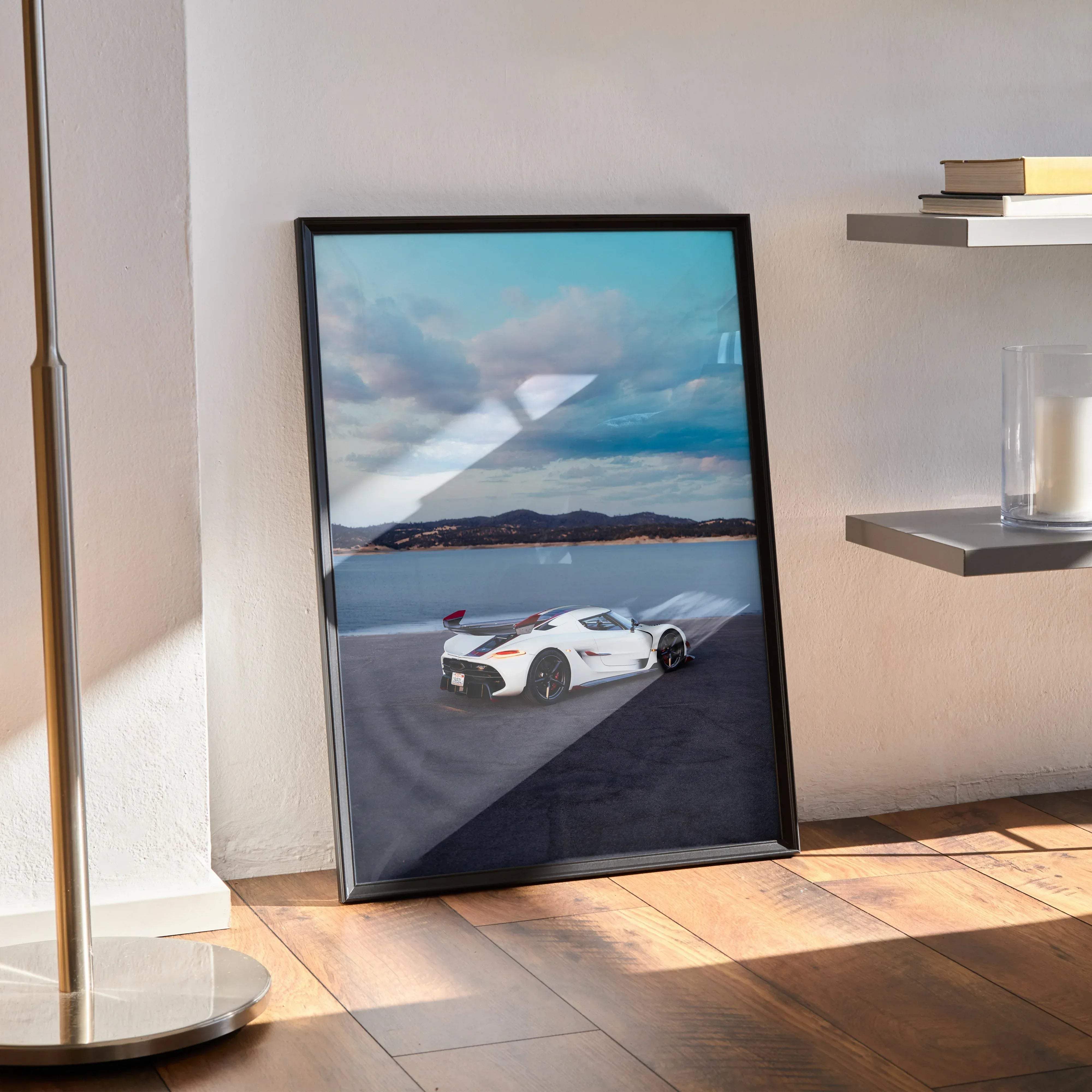 Black-framed print of a white koenigsegg jesko sports car speeding along a coastal road under a dynamic blue sky