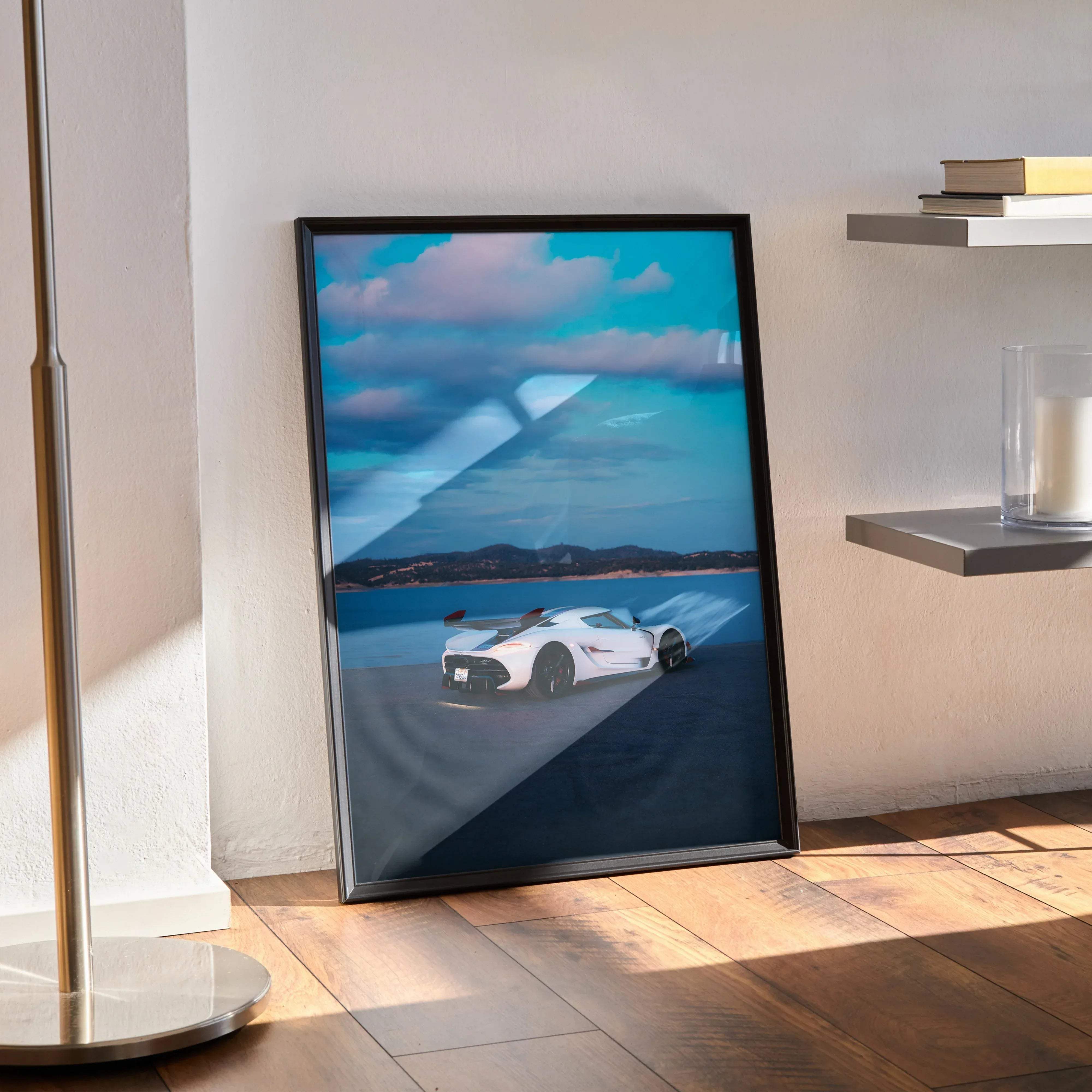 Black-framed poster of a white Koenigsegg Jesko hypercar speeding on coastal road under vibrant blue sky with clouds