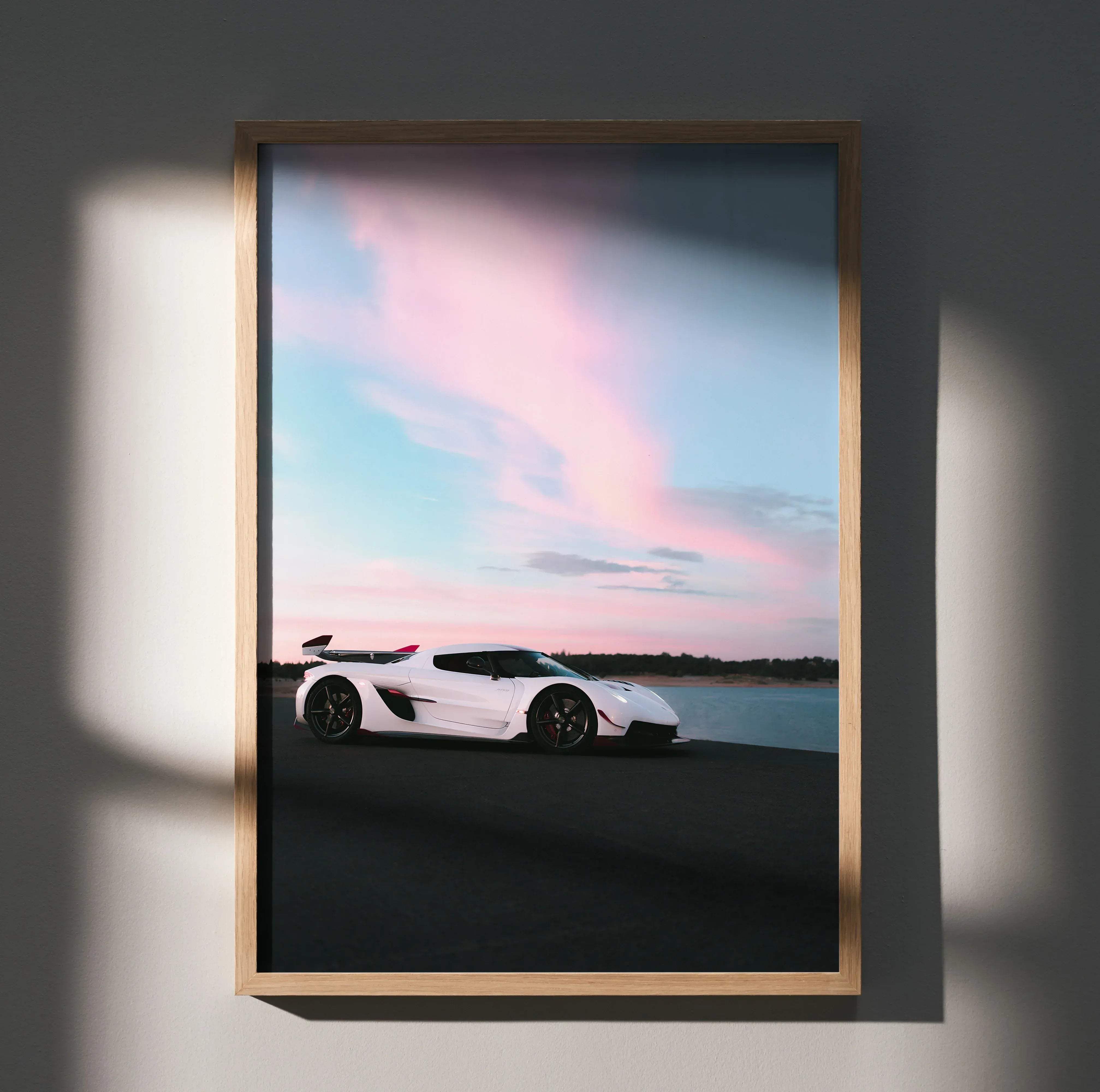 A framed high resolution poster of a white Koenigsegg Jesko sports car parked by water under a pink and blue sky