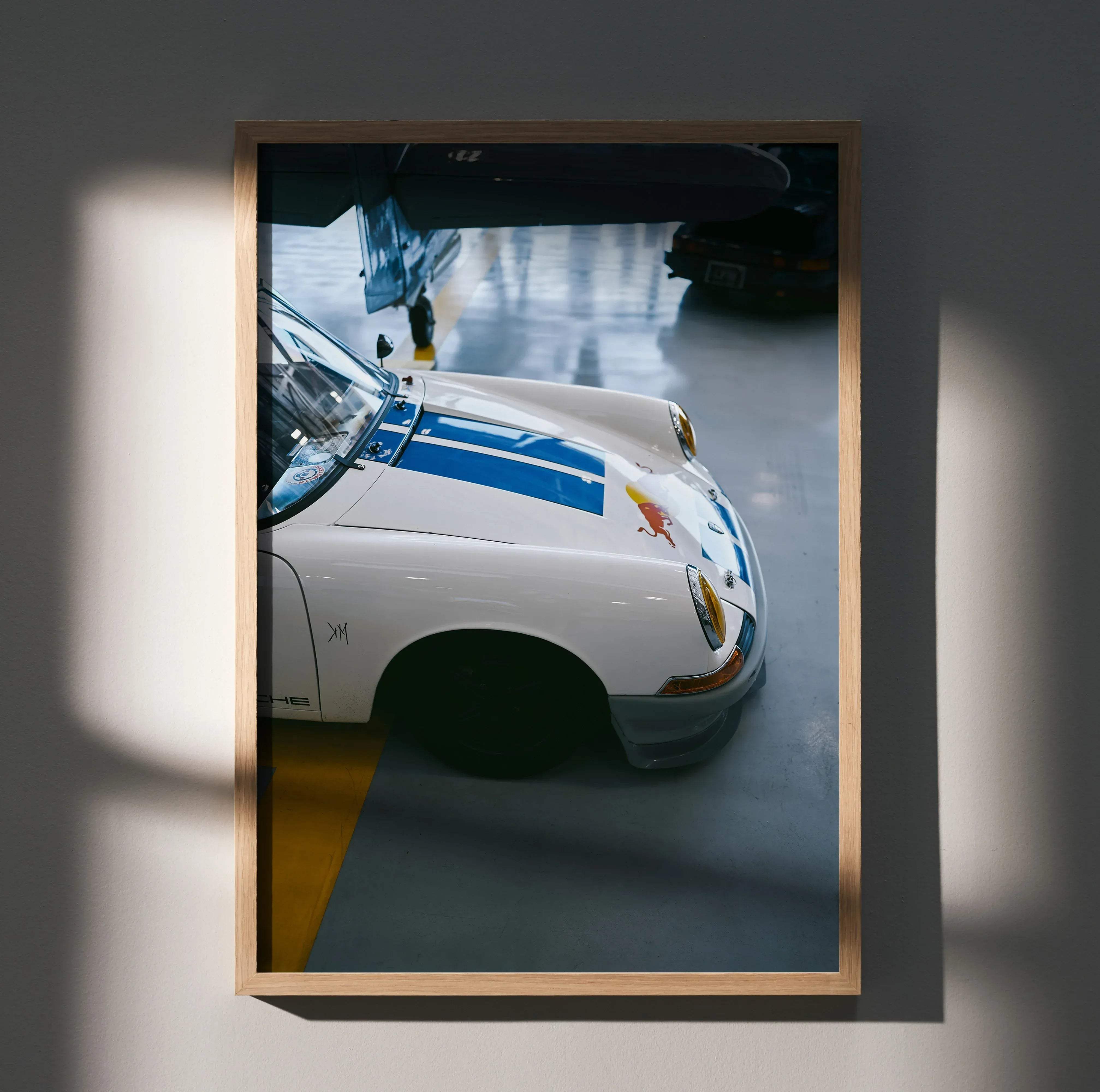 White Porsche 911 classic sports car poster with blue racing stripes and Red Bull logo framed in light wood