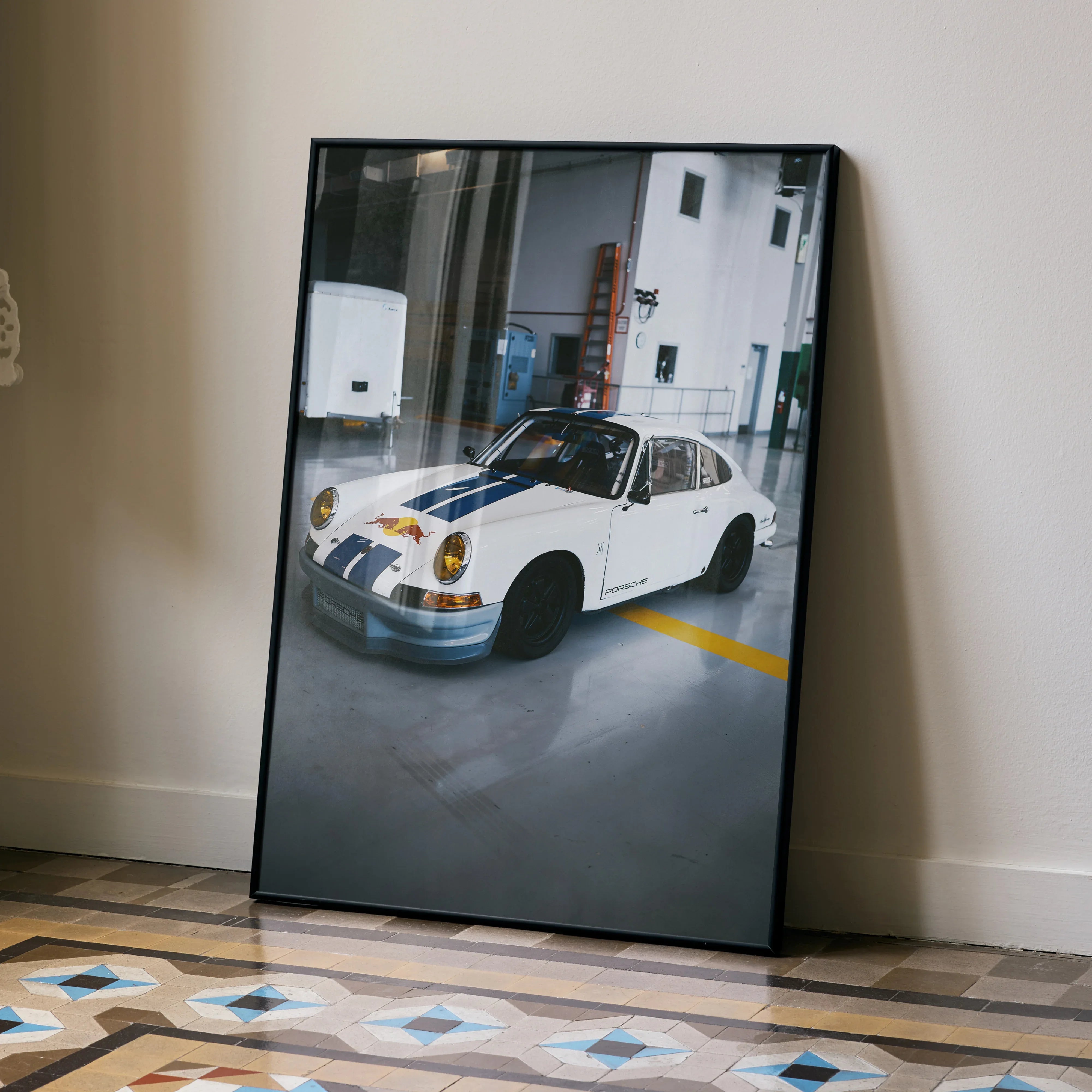 Porsche 911 classic white car poster with blue stripes leaning against beige wall wall art.