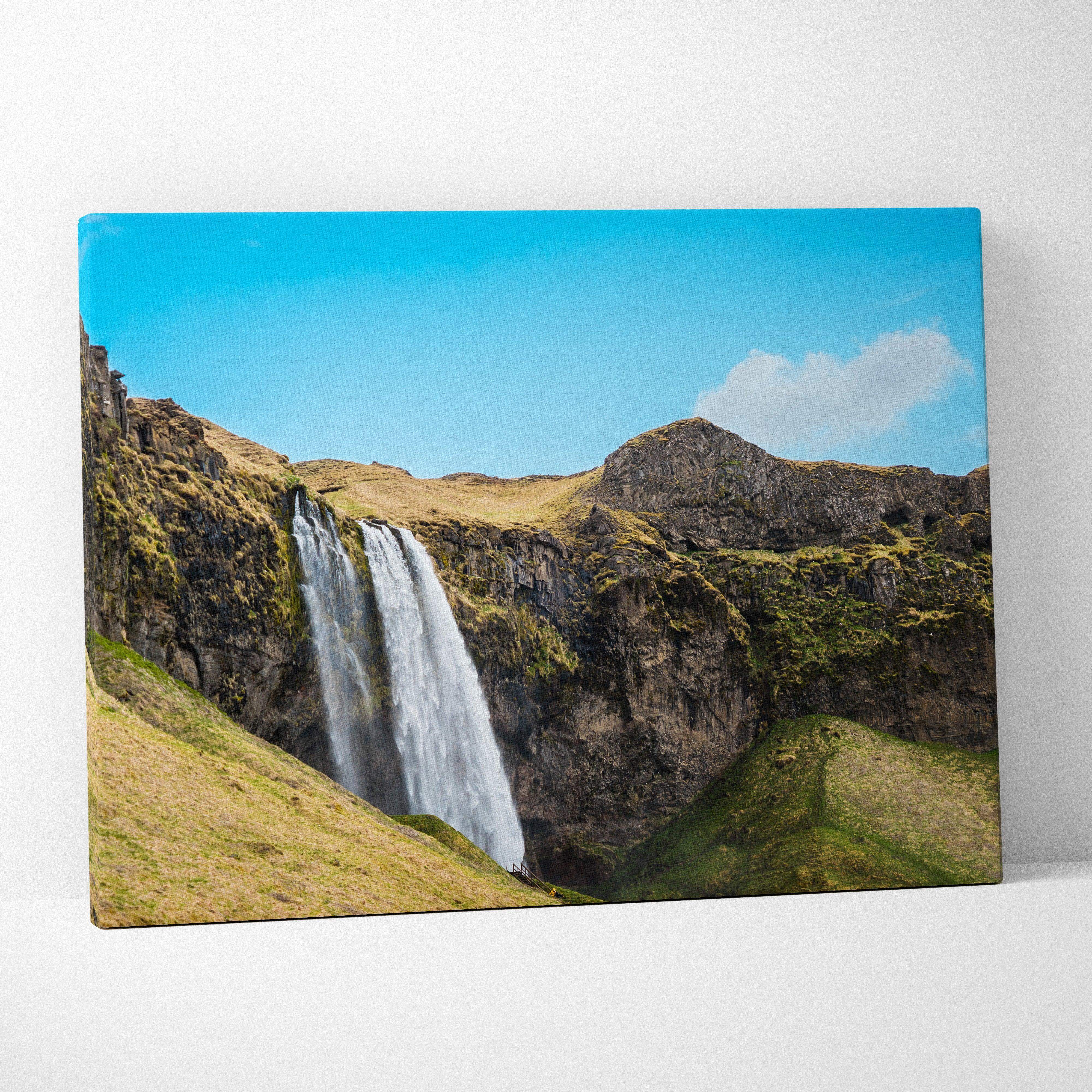 Vibrant canvas print of an icelandic waterfall cascading down mossy cliffs under a clear blue sky for living room decor