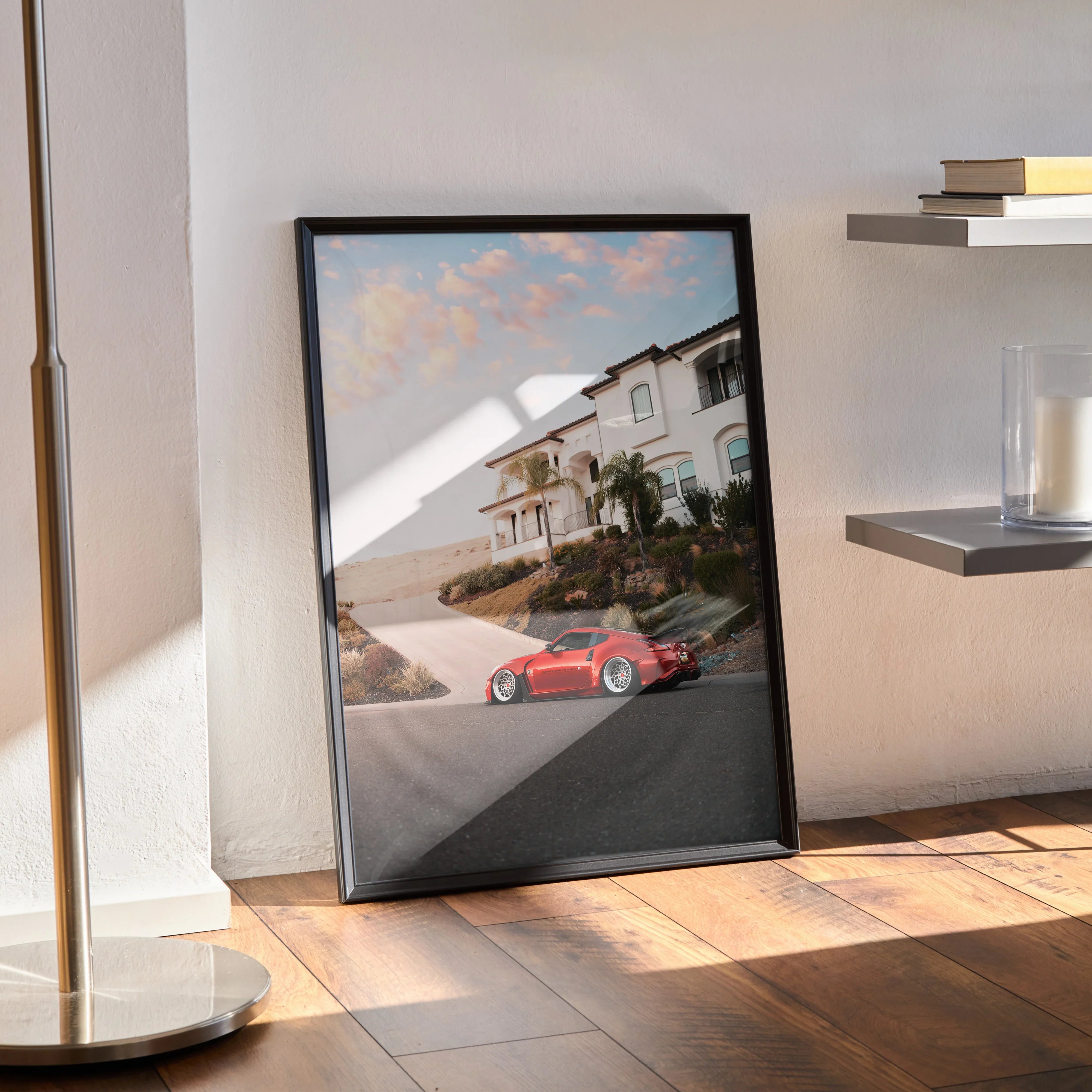 Nissan 370z poster wall art with sunset and coastal road in black frame leaning on wooden floor.