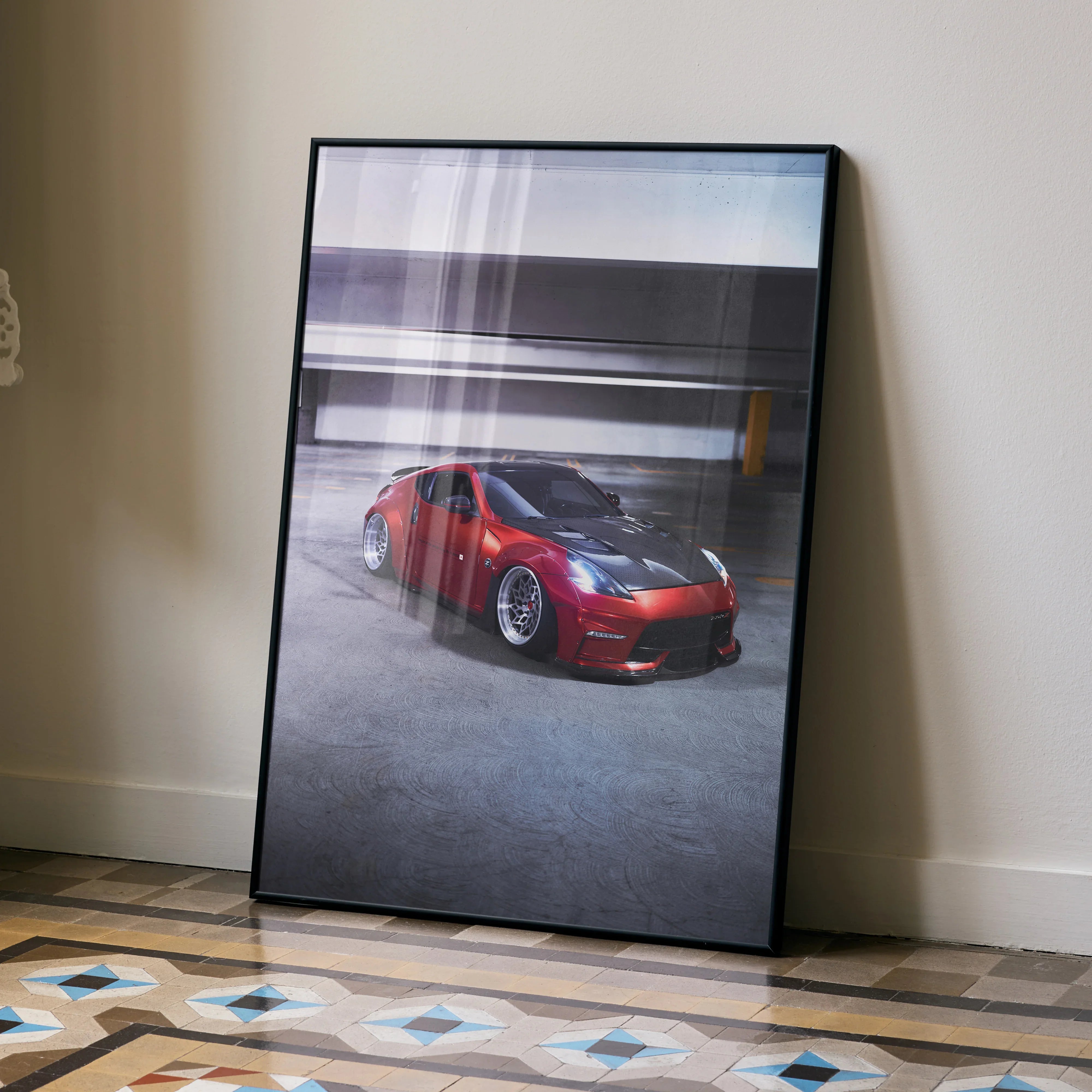Red Nissan 370Z poster in black frame leaning against wall, indoor wall art display.