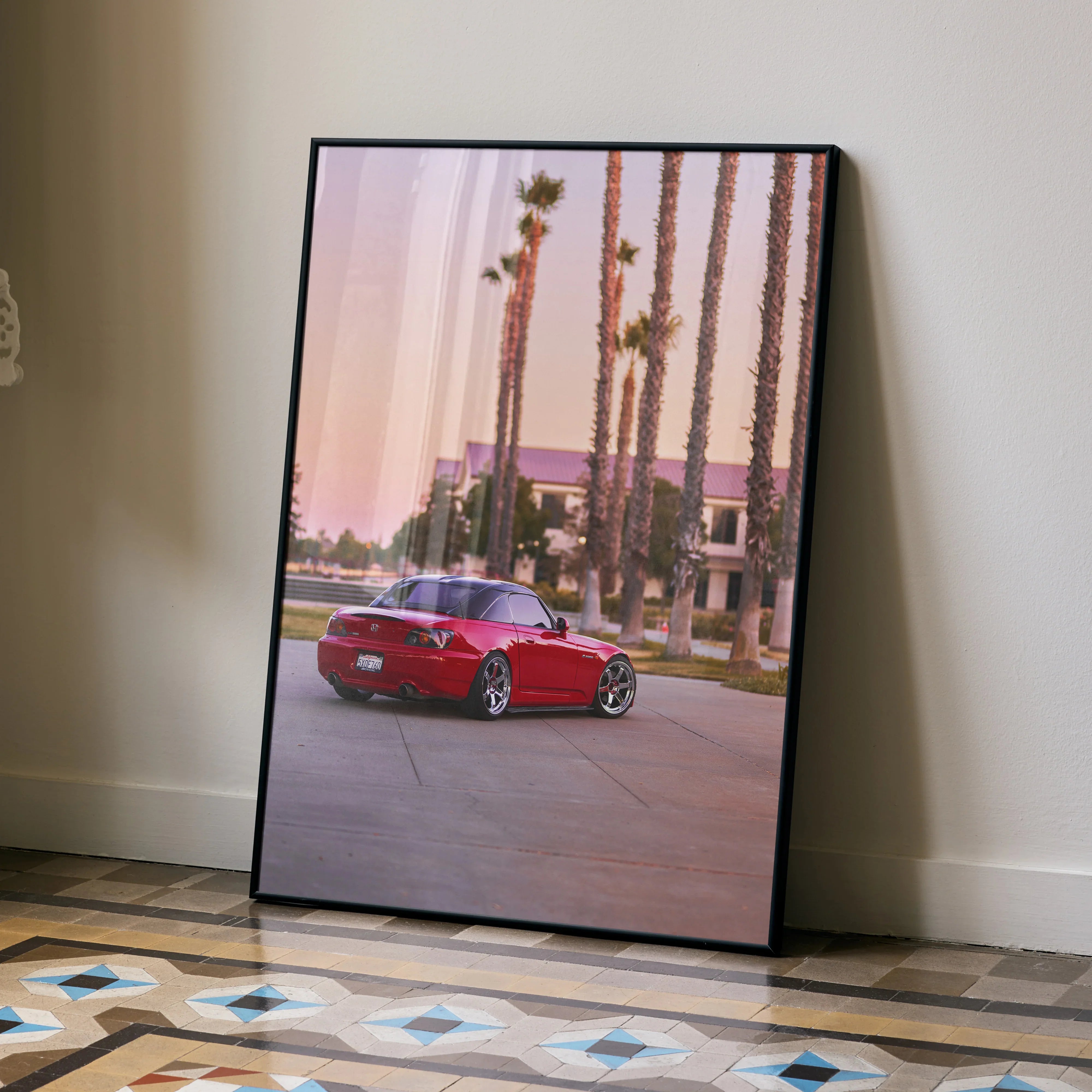 Red Honda S2000 parked by palm trees at sunset poster wall art in black frame.