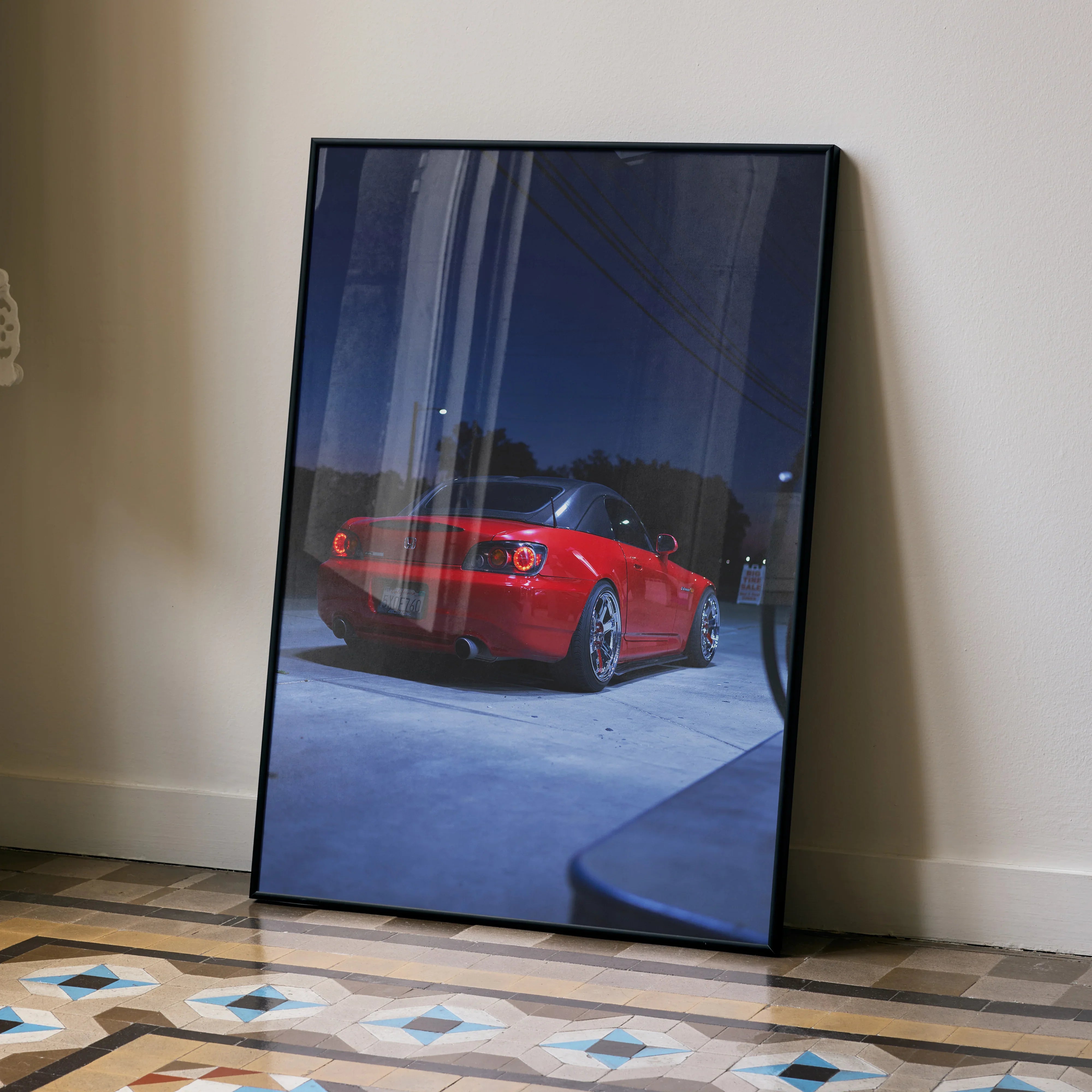 Red Honda S2000 sports car poster leaning against wall, glossy wall art in black frame.