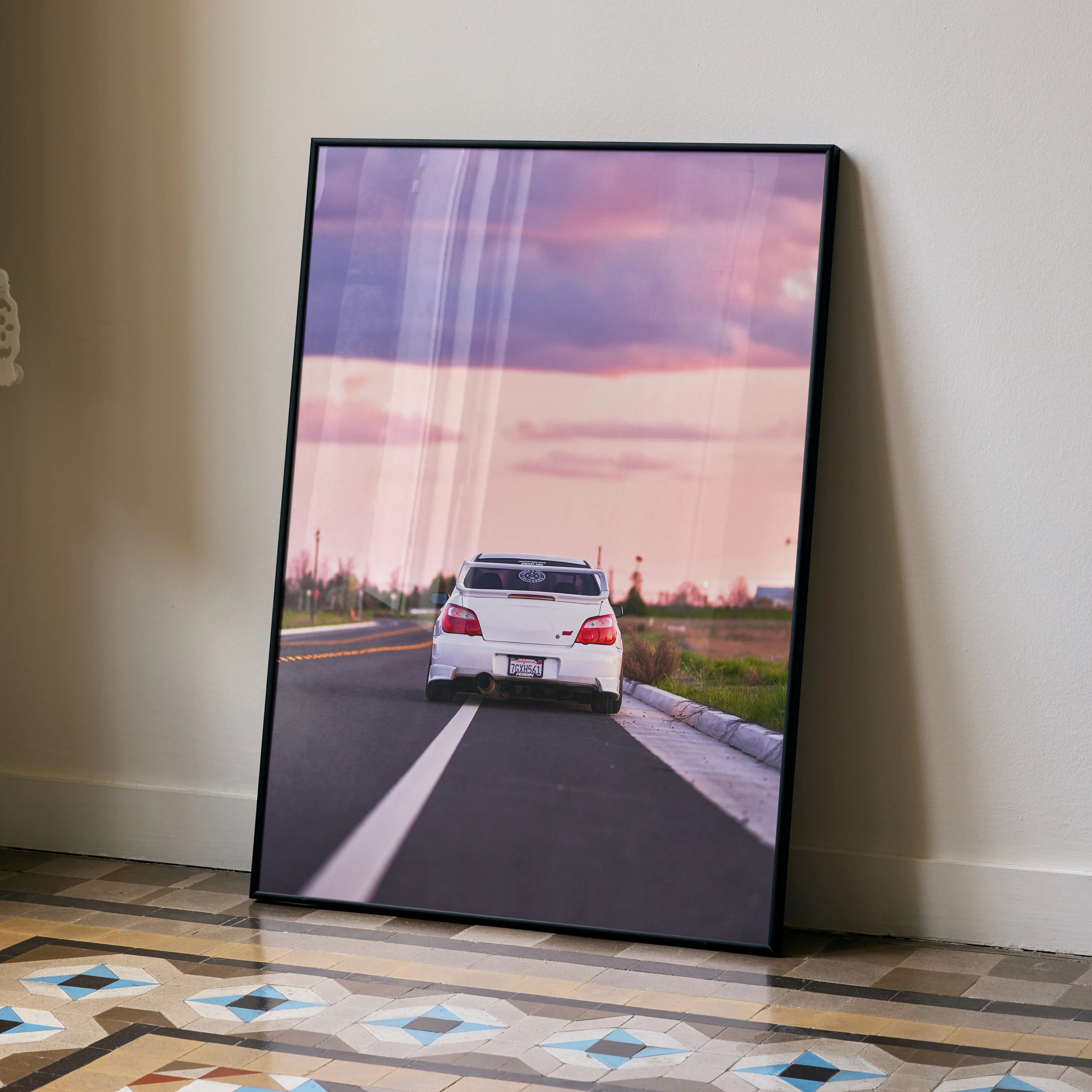 Subaru WRX STI speeding on road at sunset poster wall art in black frame on floor.