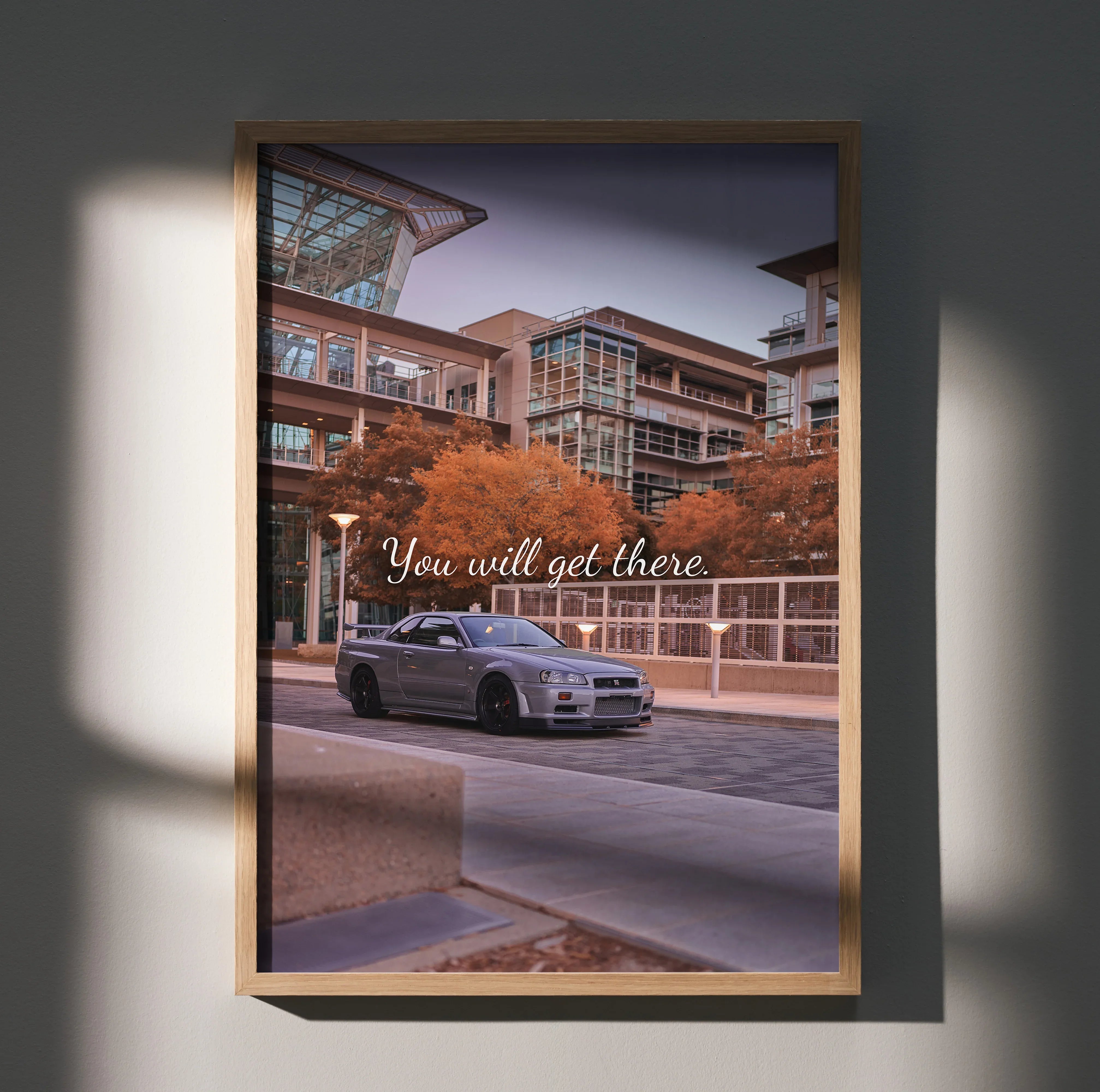 Motivational poster featuring silver Nissan R34 GT-R Skyline on city street, autumn trees, modern buildings backdrop wall art.