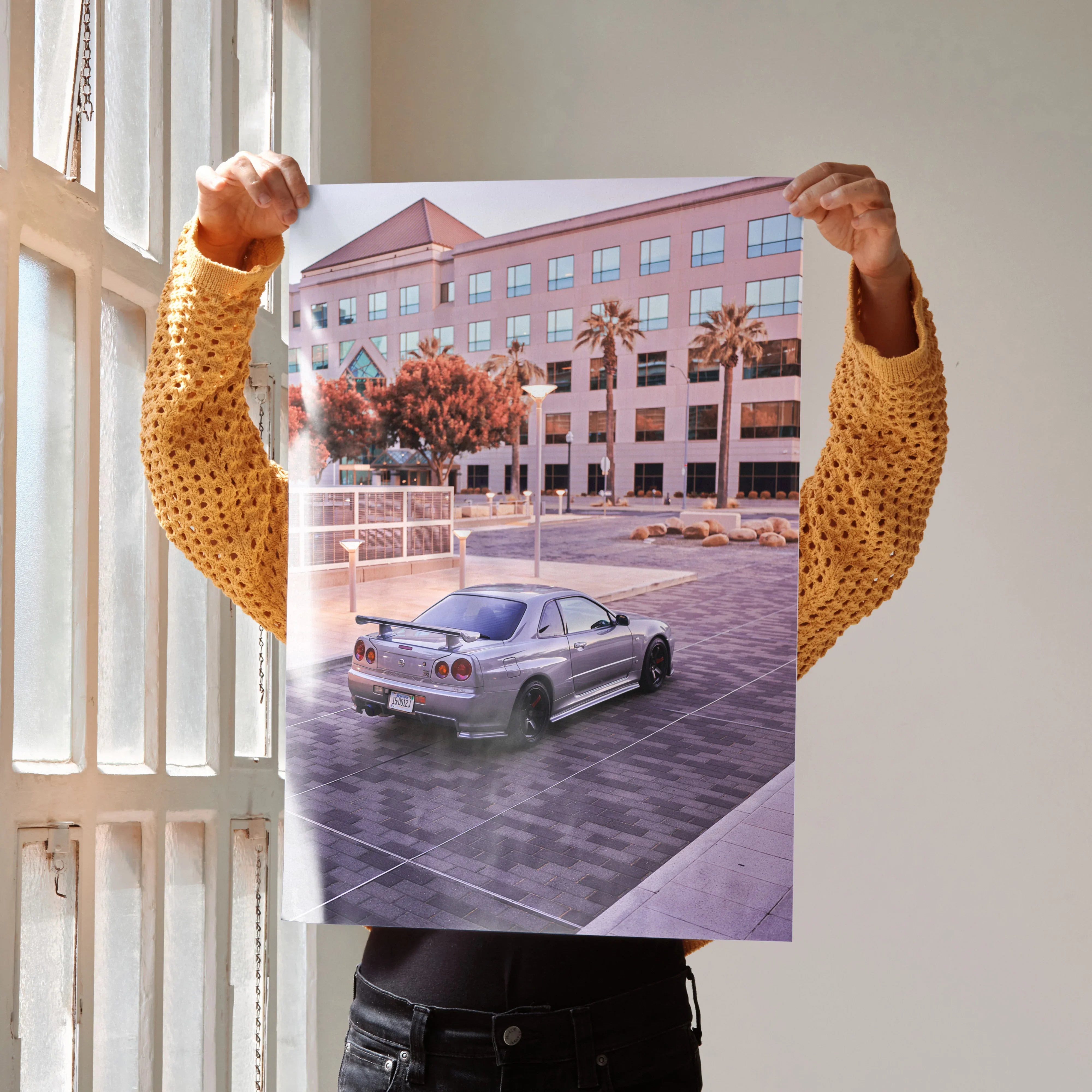Nissan R34 GTR Skyline parked in urban setting poster wall art with modern building backdrop.